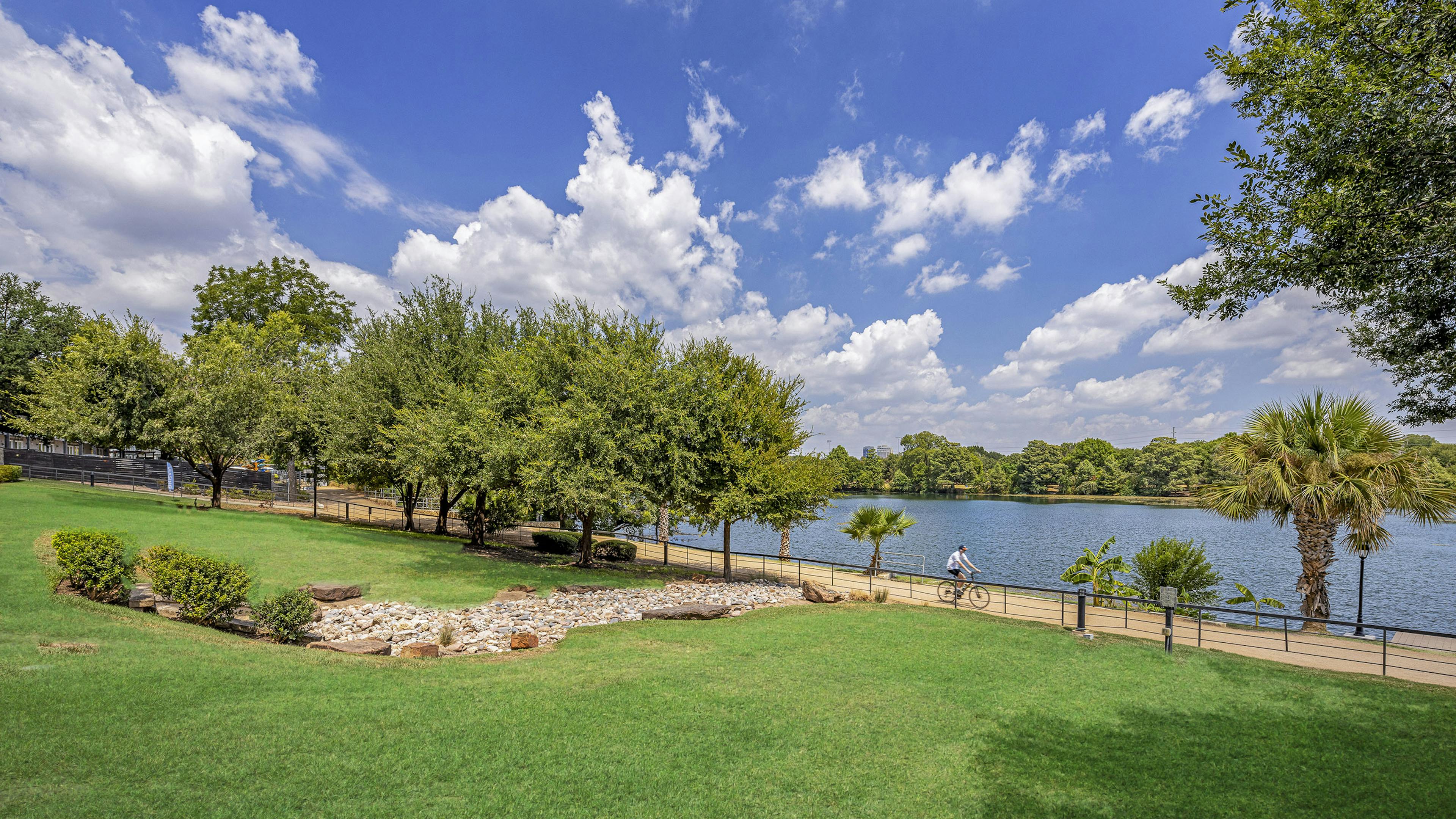 Daytime view of grass and trees along scenic Lady Bird Lake with blue sky with puffy white clouds at AMLI South Shore apartments