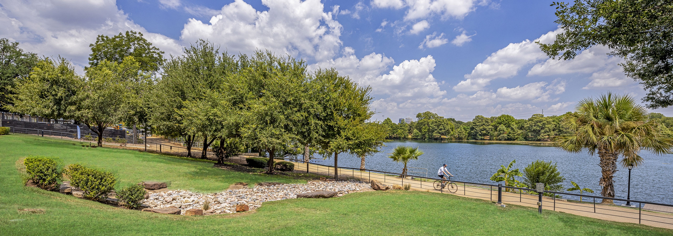 Daytime view of grass and trees along scenic Lady Bird Lake with blue sky with puffy white clouds at AMLI South Shore apartments