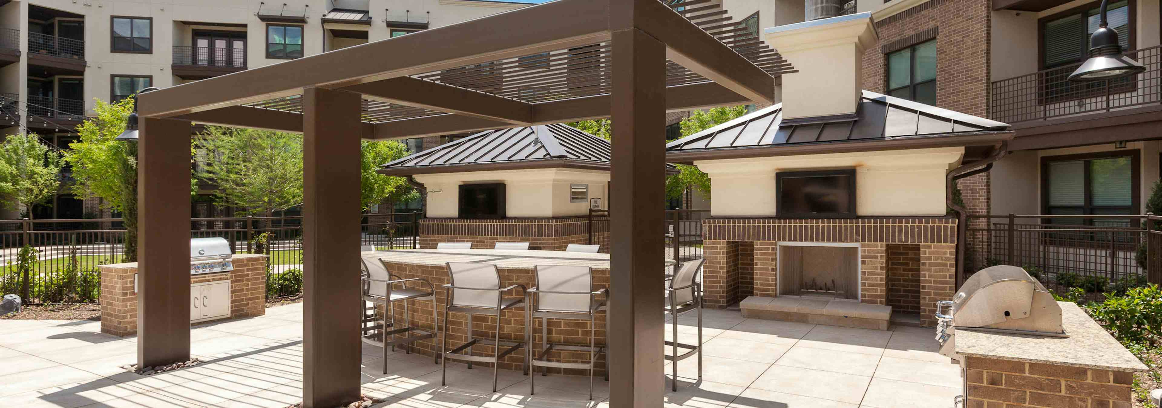 Daytime view of two grills, outdoor fireplace, table and seating at AMLI at the Ballpark apartment building