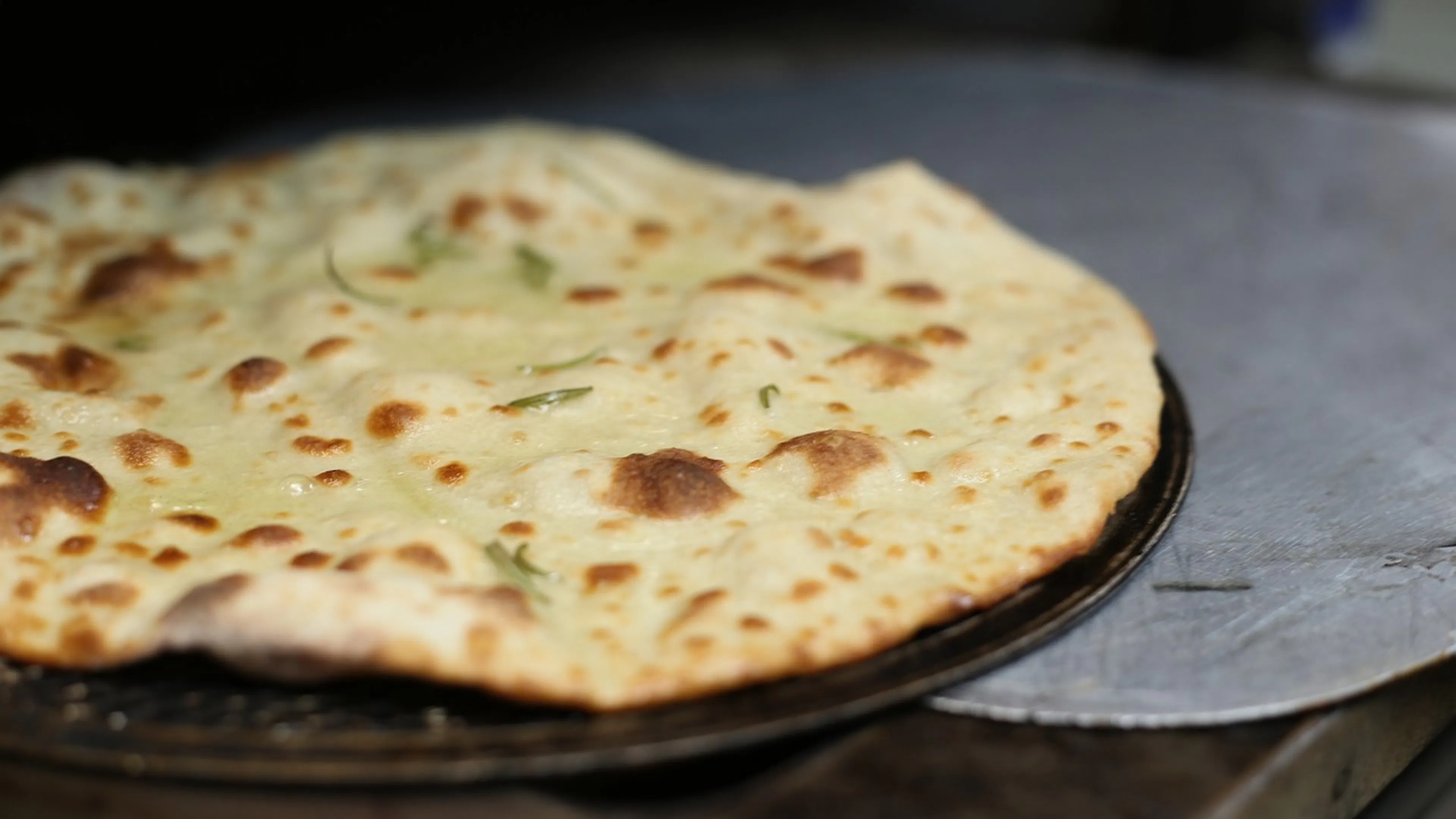 A close up of naan bread served on a dark plate with bits of cilantro sprinkled on top
