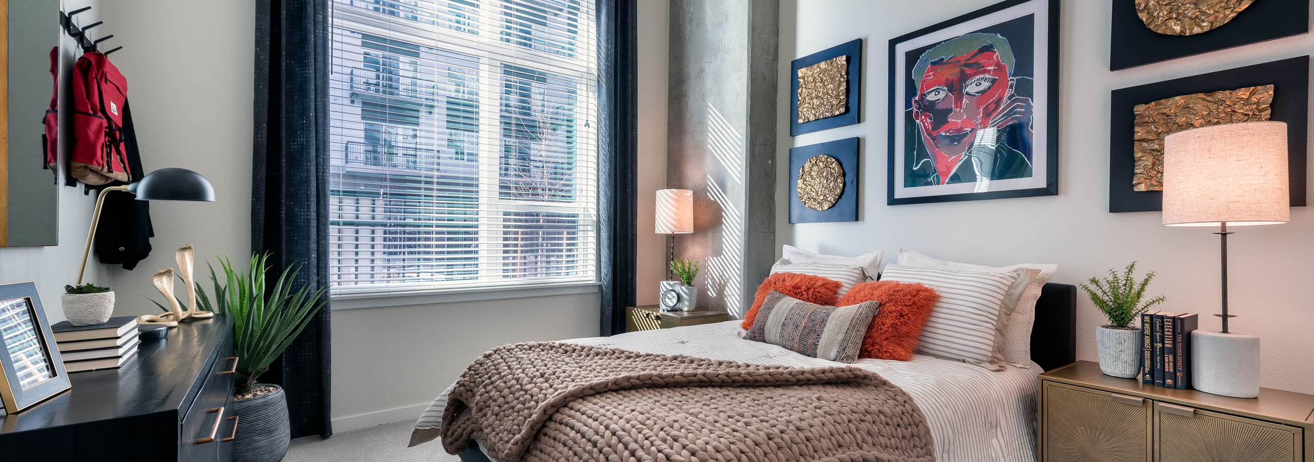 Interior view of a bedroom at AMLI Art District with a bed and large throw blanket and dresser with art pieces on the wall