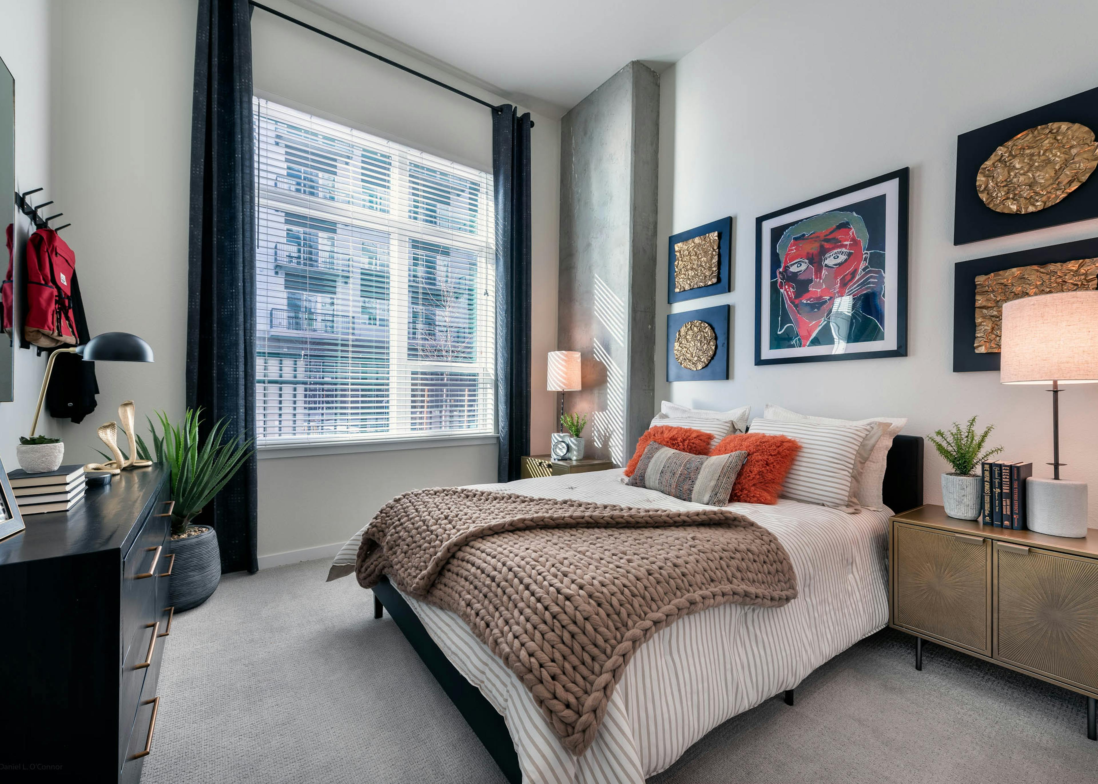 Interior view of a bedroom at AMLI Art District with a bed and large throw blanket and dresser with art pieces on the wall