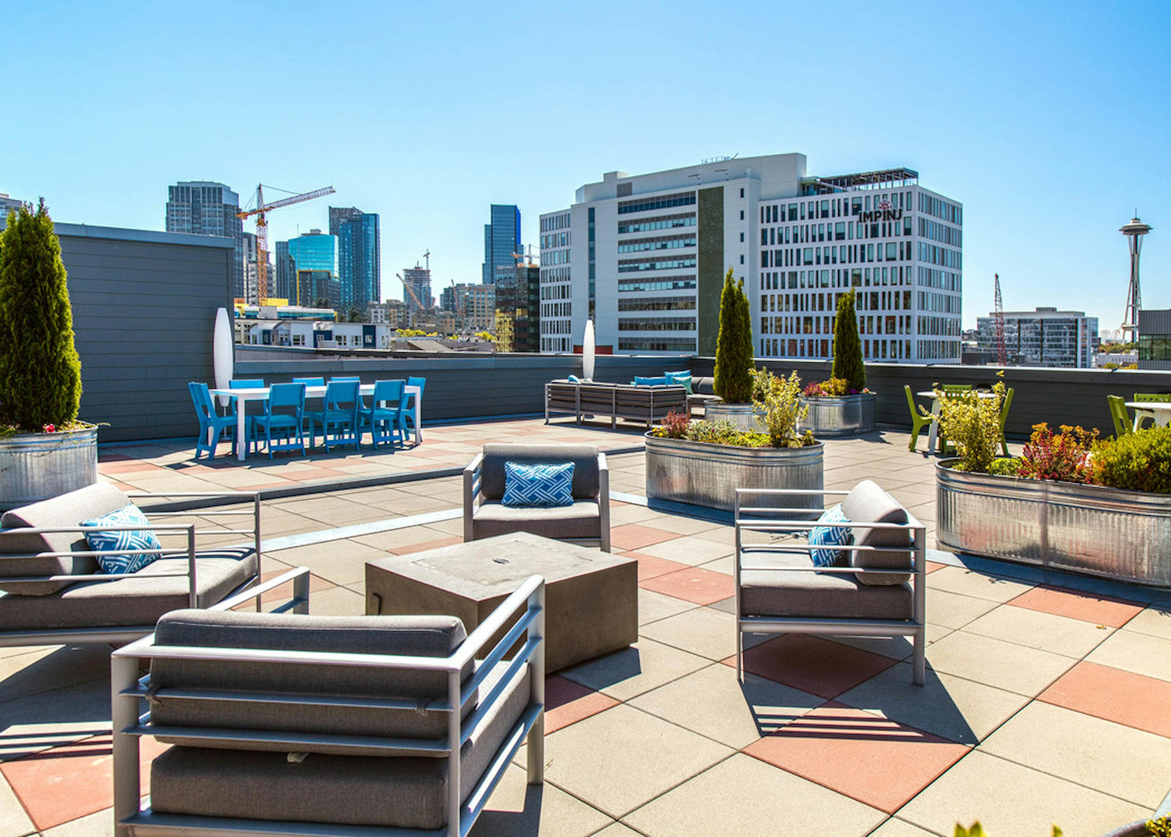 Daytime view of AMLI 535 rooftop deck with patio furniture fire pit bushes and view of Space Needle and downtown Seattle