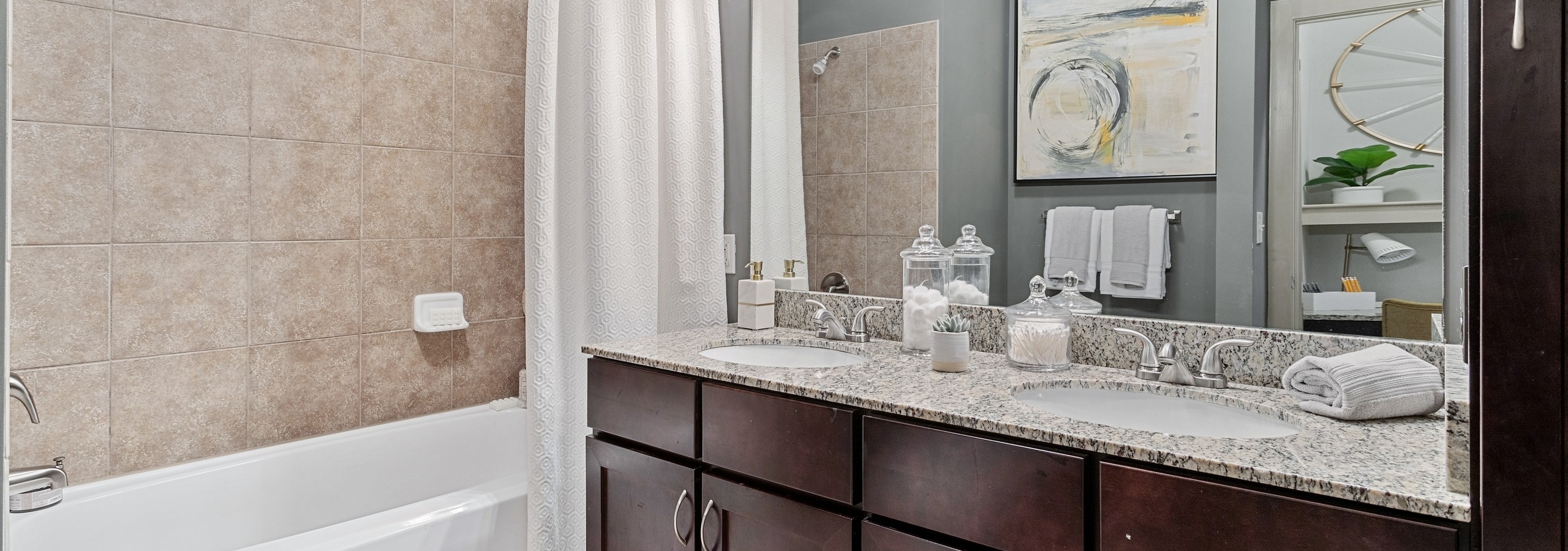 Interior view of bathroom with dark double vanity with granite counters and wall mirror and soaking tub at AMLI Parkside