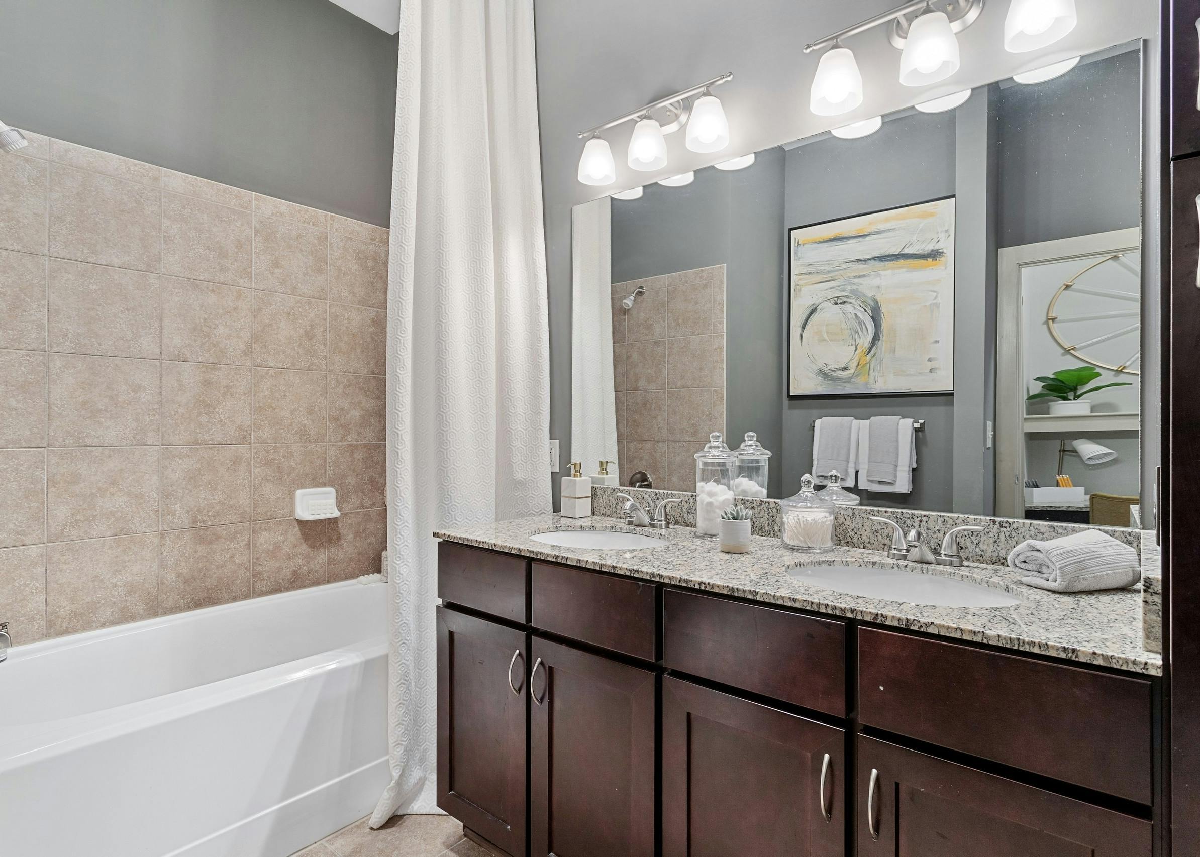 Interior view of bathroom with dark double vanity with granite counters and wall mirror and soaking tub at AMLI Parkside