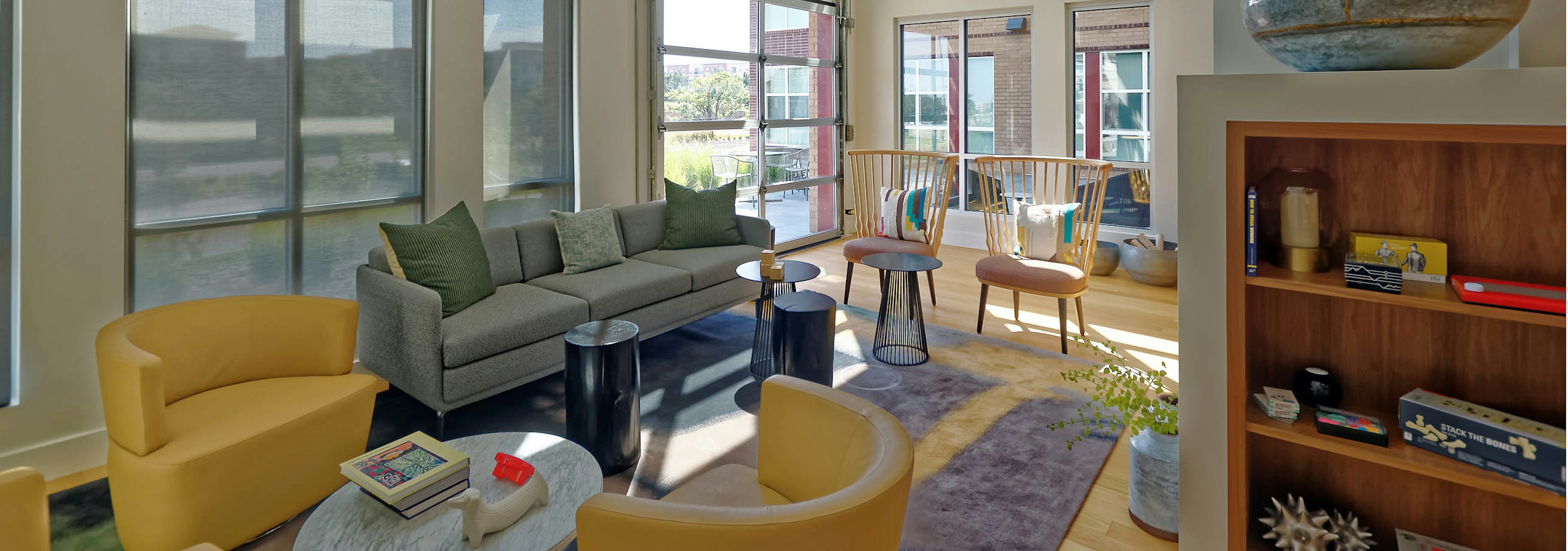 A resident lounge at AMLI Dry Creek apartments with a book shelve and several chairs and a couch with a view of the rooftop