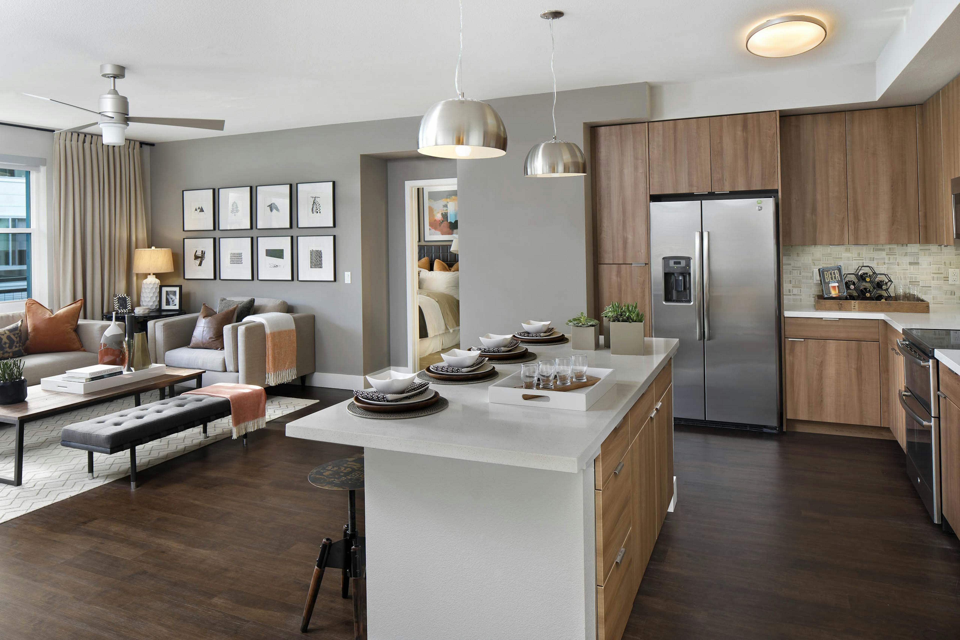 Interior of AMLI Uptown Orange apartment kitchen with quartz counters flowing into a furnished living room with ceiling fan