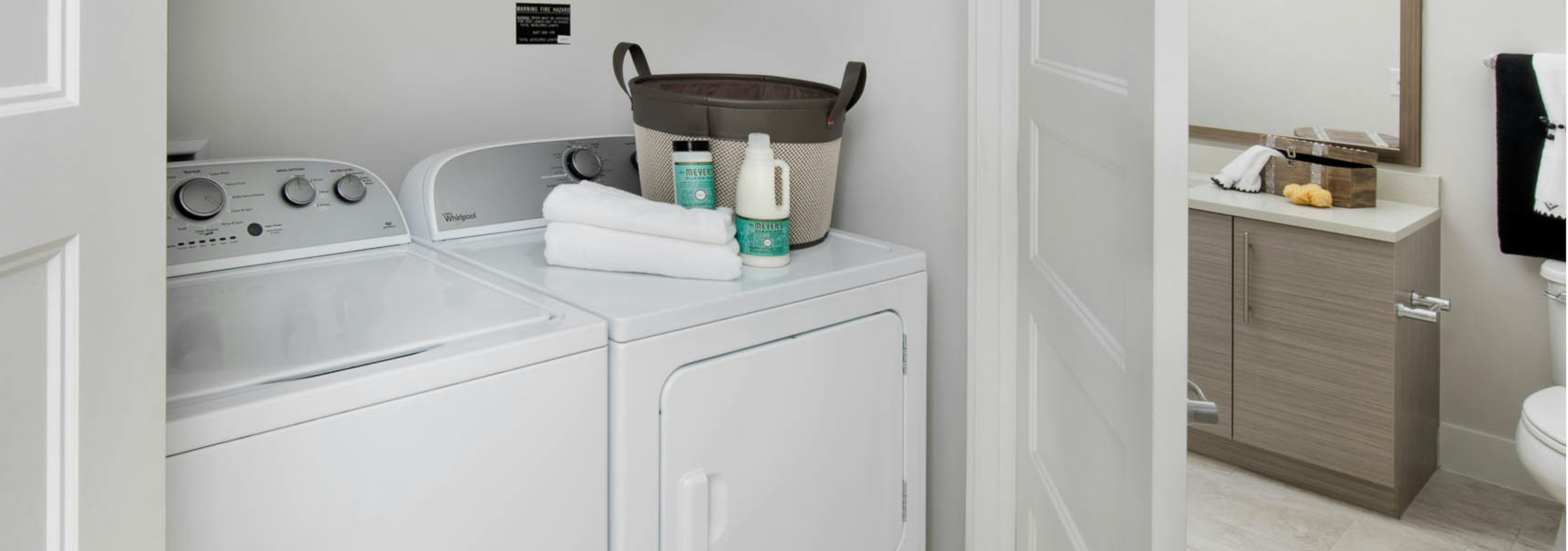 AMLI Buckhead laundry machines with a basket and towel resting on the dryer and a door peaking open leading into the bathroom