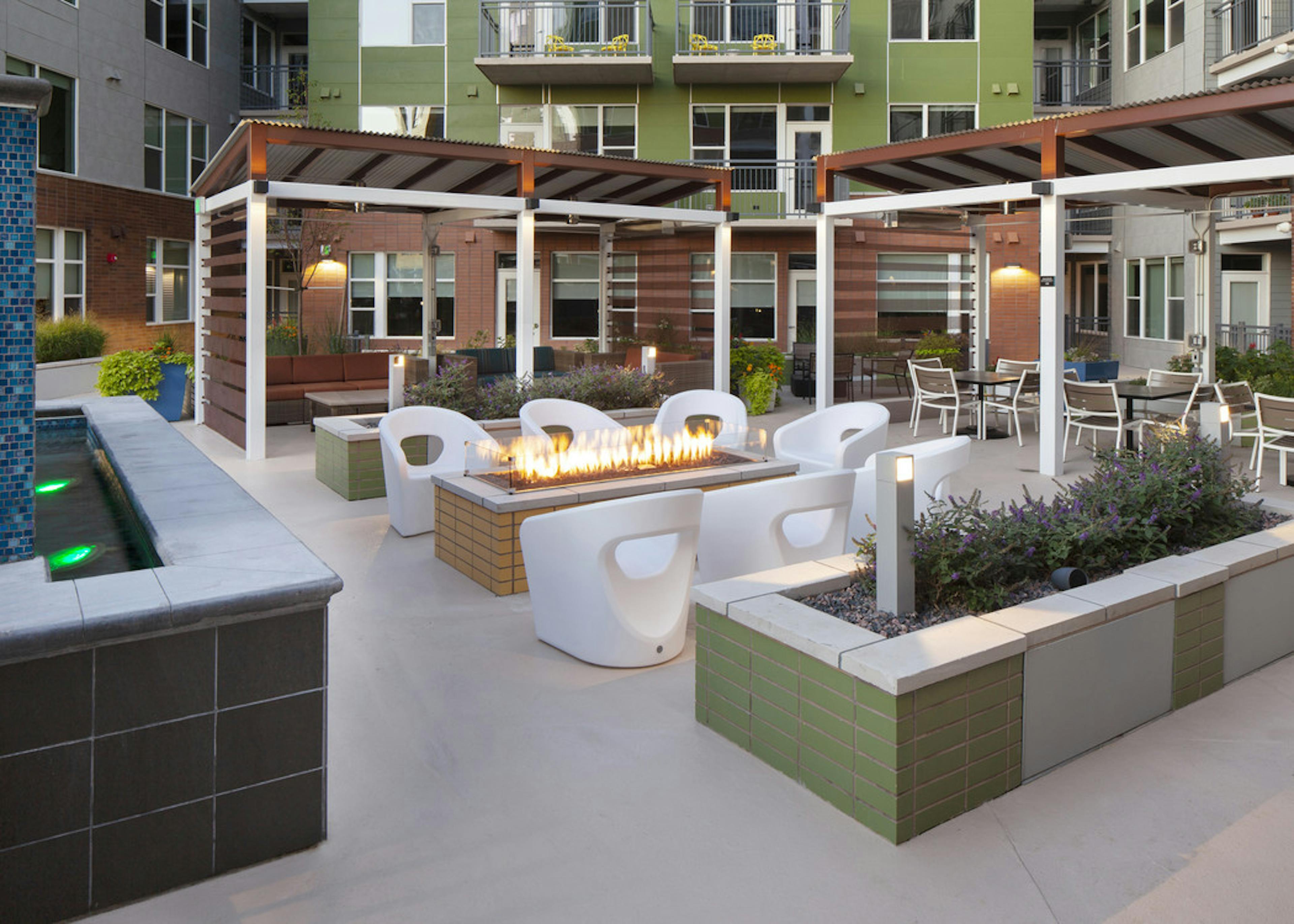 Night time view of rooftop area at AMLI Riverfront Green apartments with fire pit featured with chairs and planter boxes