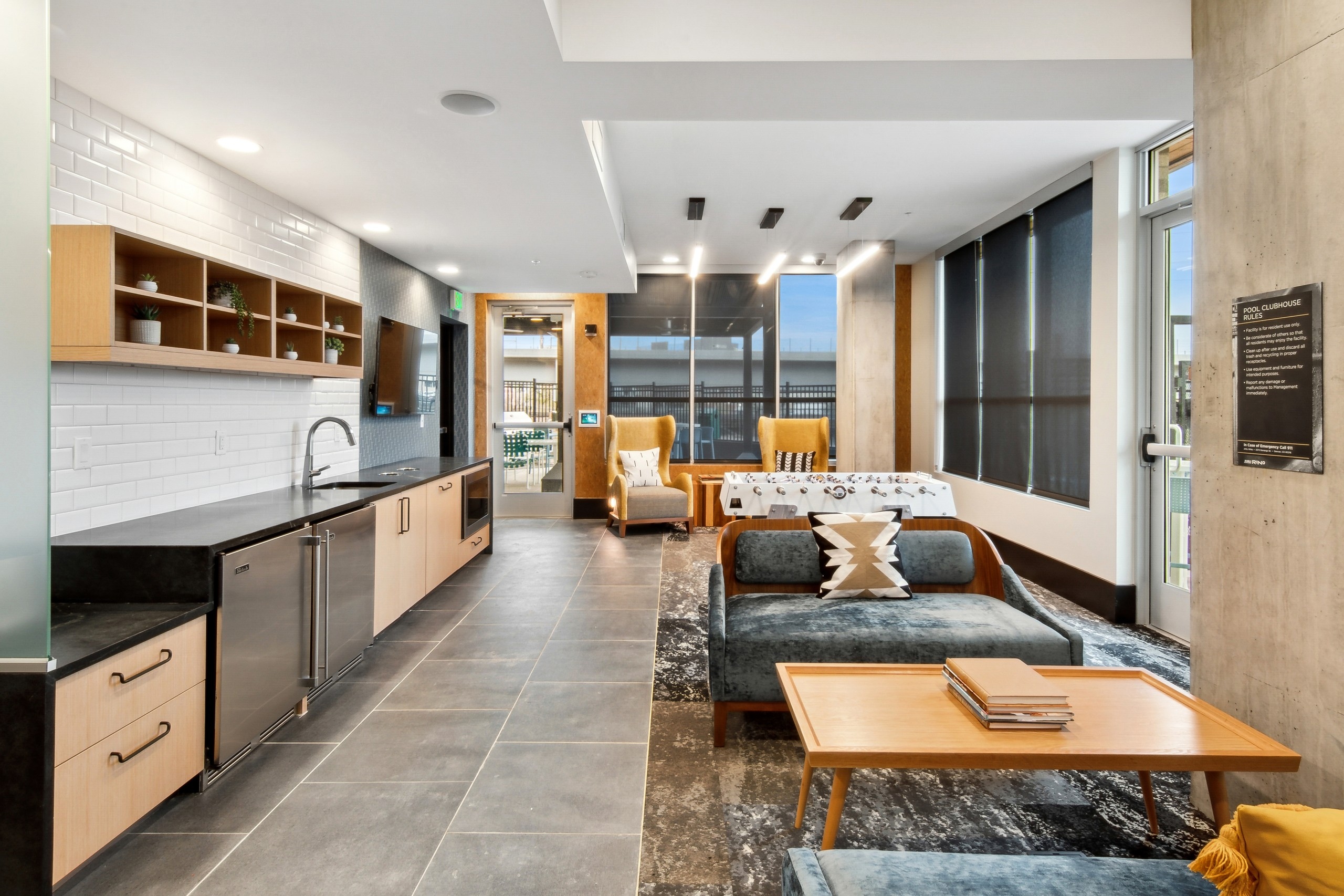 Pool clubhouse at AMLI RiNo with comfy seating and a large black serving kitchen countertop with a white tile backsplash  