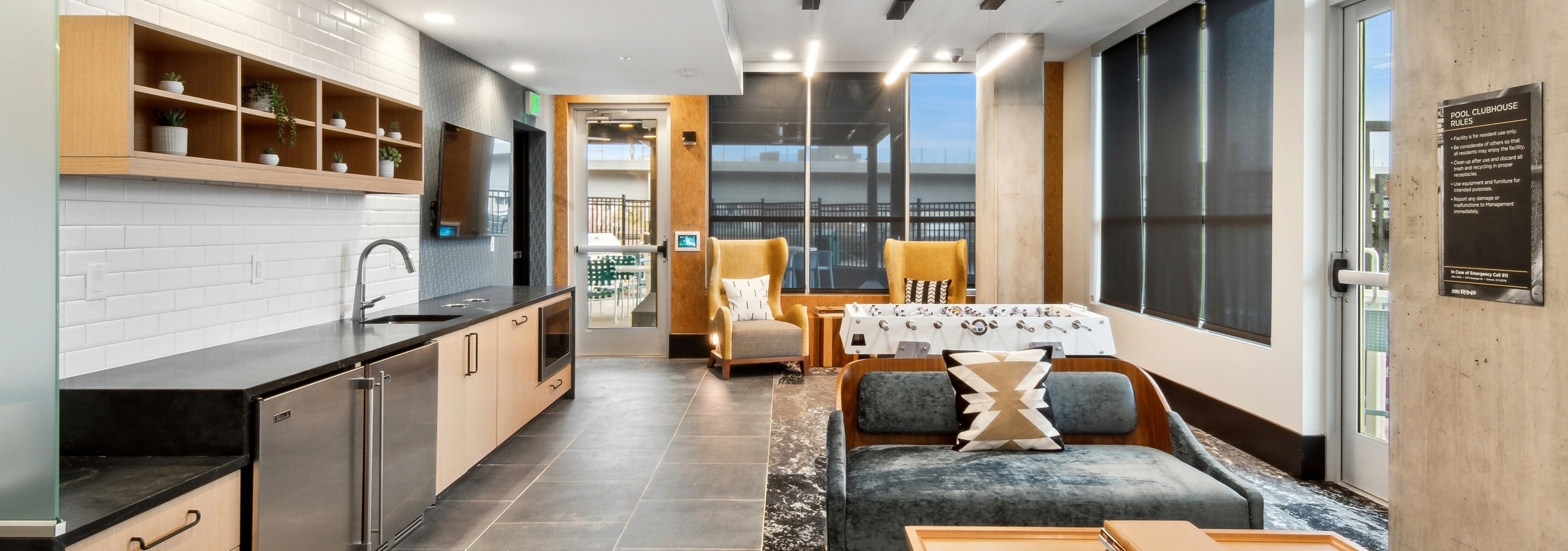 Pool clubhouse at AMLI RiNo with comfy seating and a large black serving kitchen countertop with a white tile backsplash