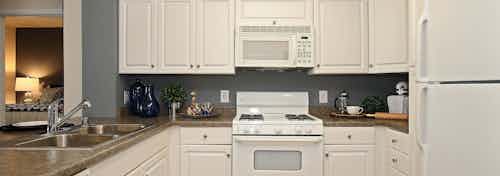 Interior of AMLI Warner Center apartment kitchen with white cabinetry, double sink and white appliances and peek into bedroom