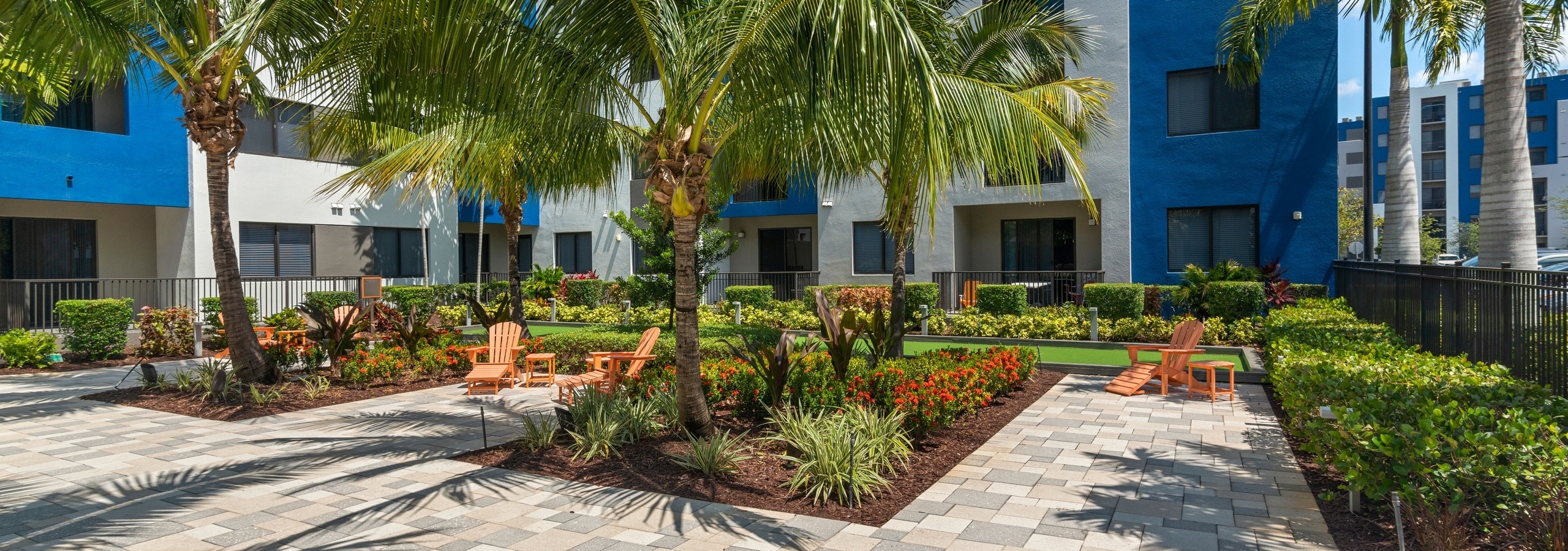 AMLI 8800 apartment building courtyard with lush tropical landscape and faux grass bocce ball court and orange armchairs