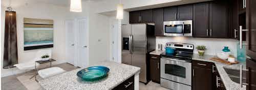 Interior view of AMLI Doral apartment kitchen area with island, stainless steel appliances,light fixture and granite counters