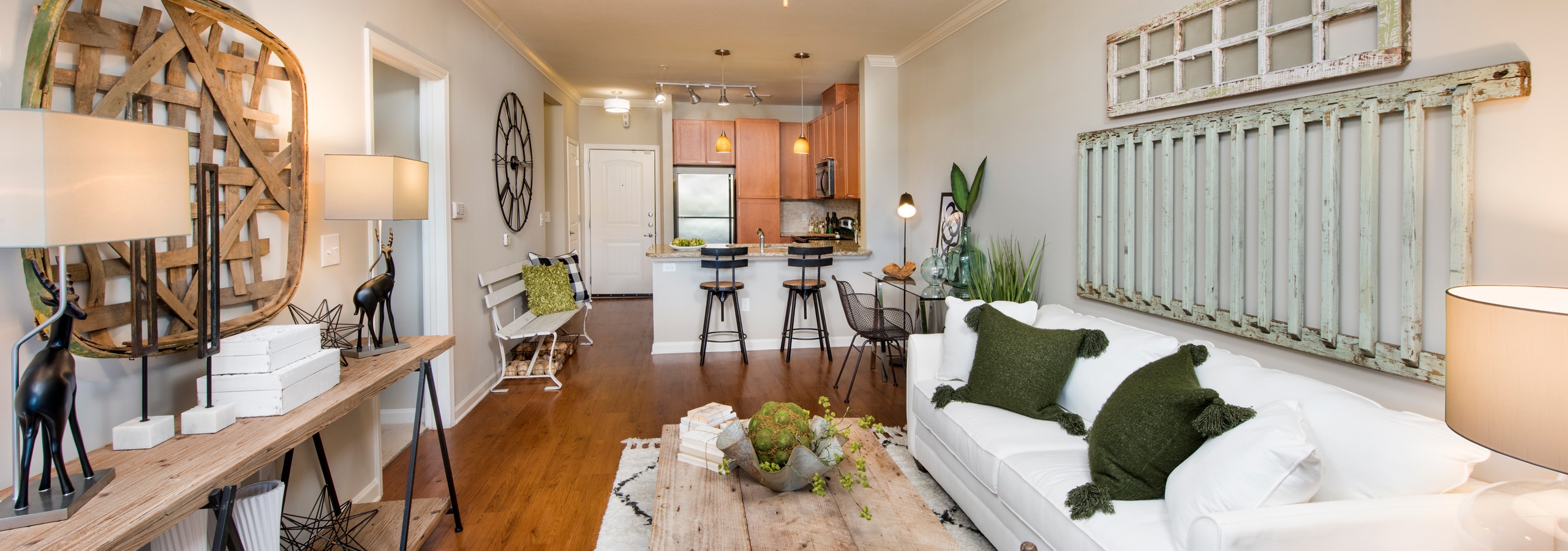AMLI North Point living room with rustic decor and medium colored wood floors which connect to kitchen area in the background