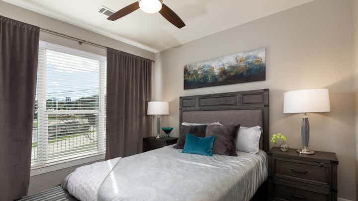 AMLI South Shore bedroom showing bed with grey headboard and pillows with white sheets and window on the left with matching grey curtains