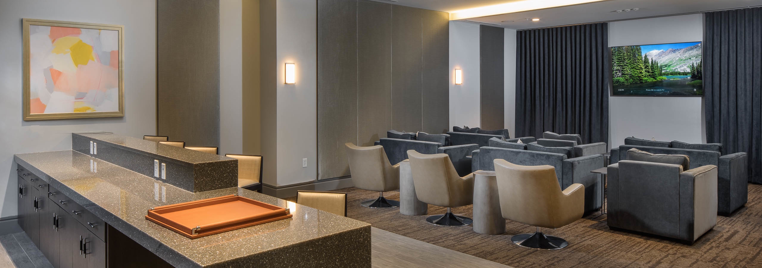 Interior of theatre at AMLI 3464 with grey seating facing large TV on the wall with a curtain and a kitchen area in the back