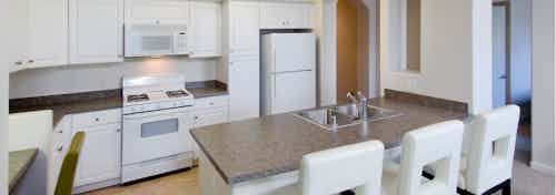 Interior view of AMLI Warner Center vacant apartment kitchen with white cabinetry and white appliances and white bar stools