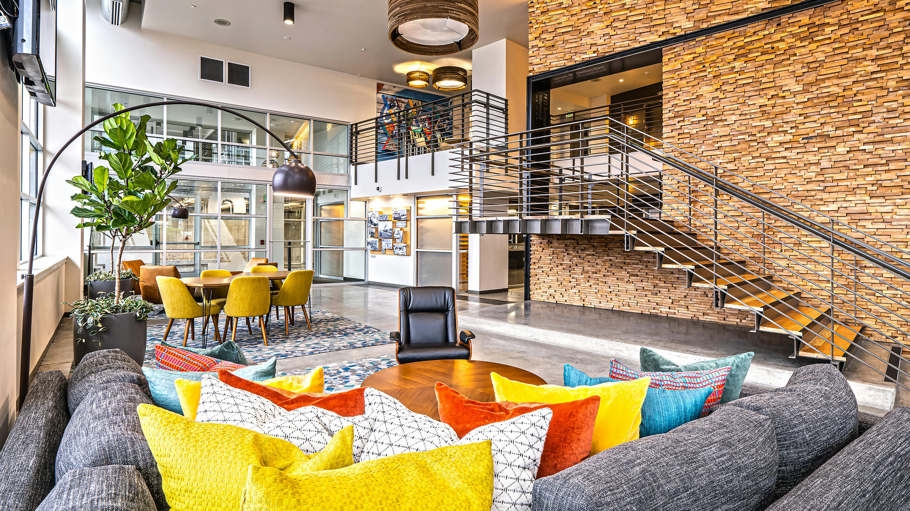 AMLI Mark24 two-story lobby with cozy seating areas and stone wall behind metal staircase and glass door and windows in rear