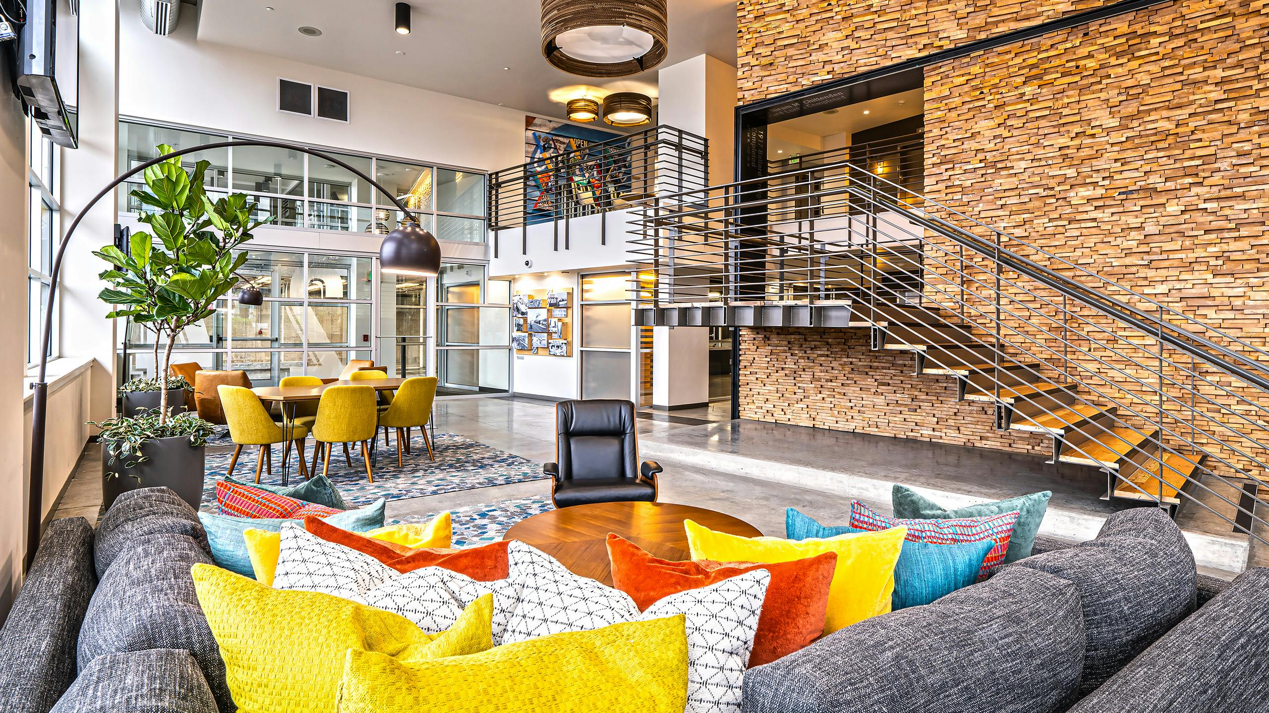 AMLI Mark24 two-story lobby with cozy seating areas and stone wall behind metal staircase and glass door and windows in rear