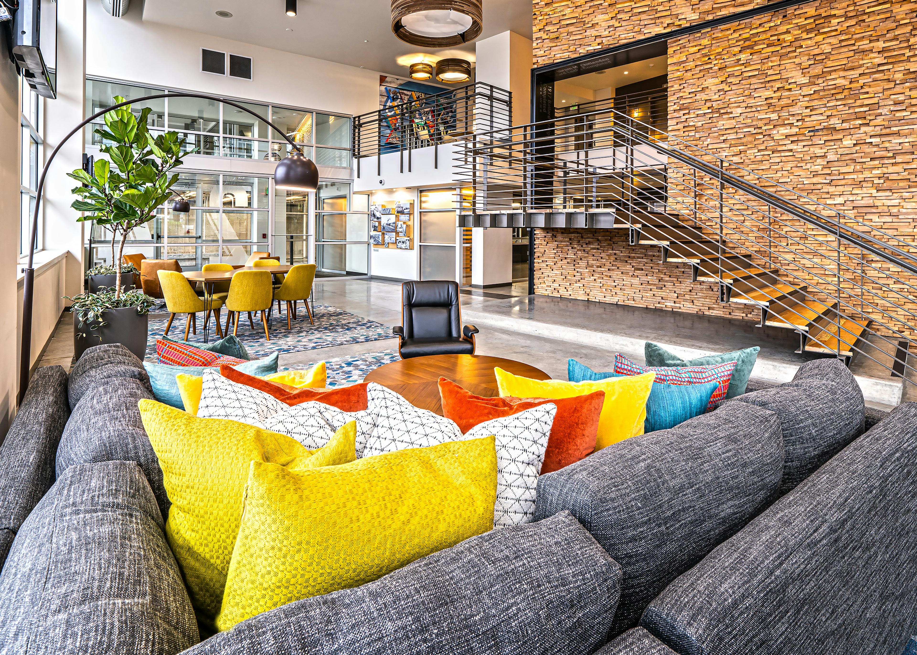 AMLI Mark24 two-story lobby with cozy seating areas and stone wall behind metal staircase and glass door and windows in rear