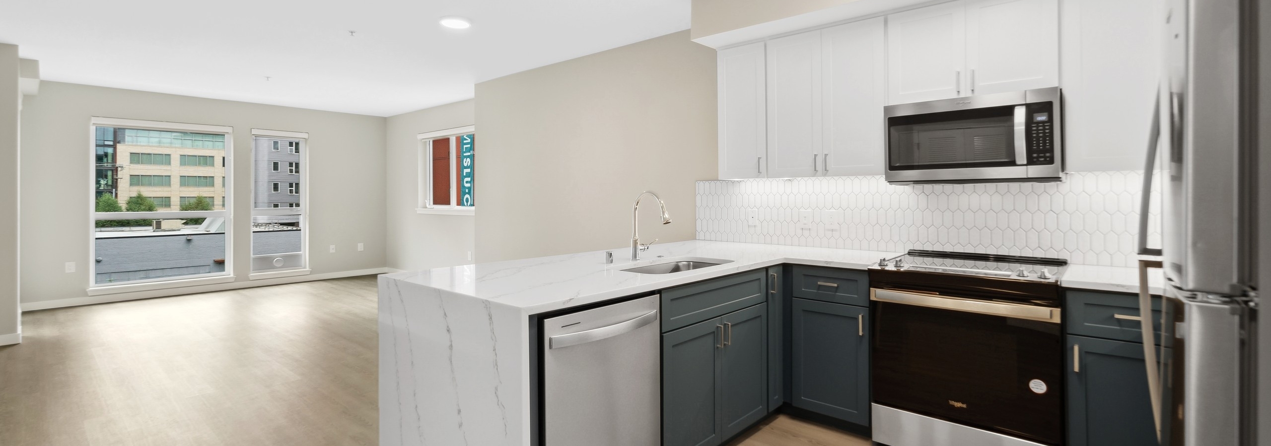 Kitchen at AMLI 535 with quartz countertop and stainless steel refrigerator and a view into living room with plank flooring
