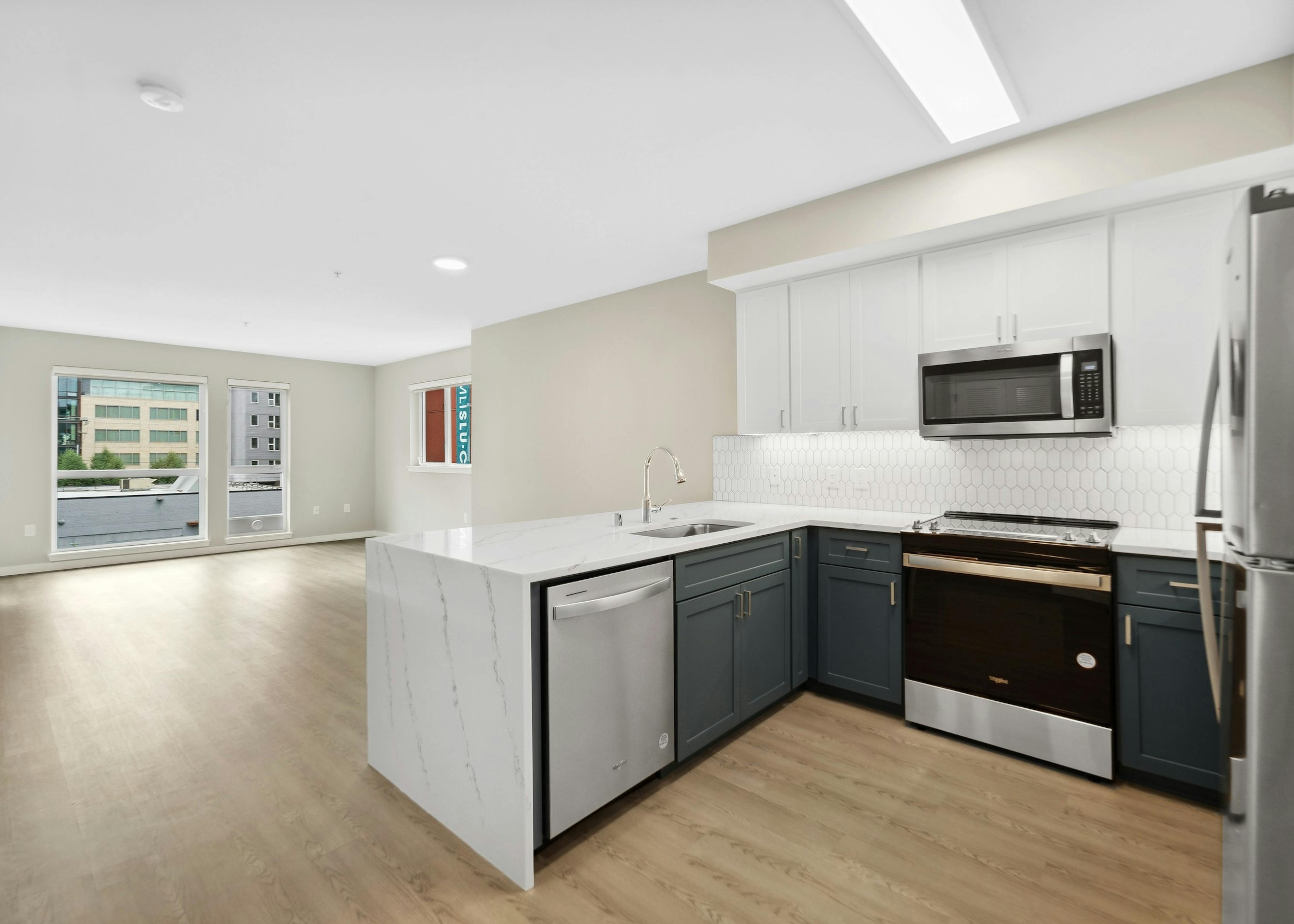 Kitchen at AMLI 535 with quartz countertop and stainless steel refrigerator and a view into living room with plank flooring
