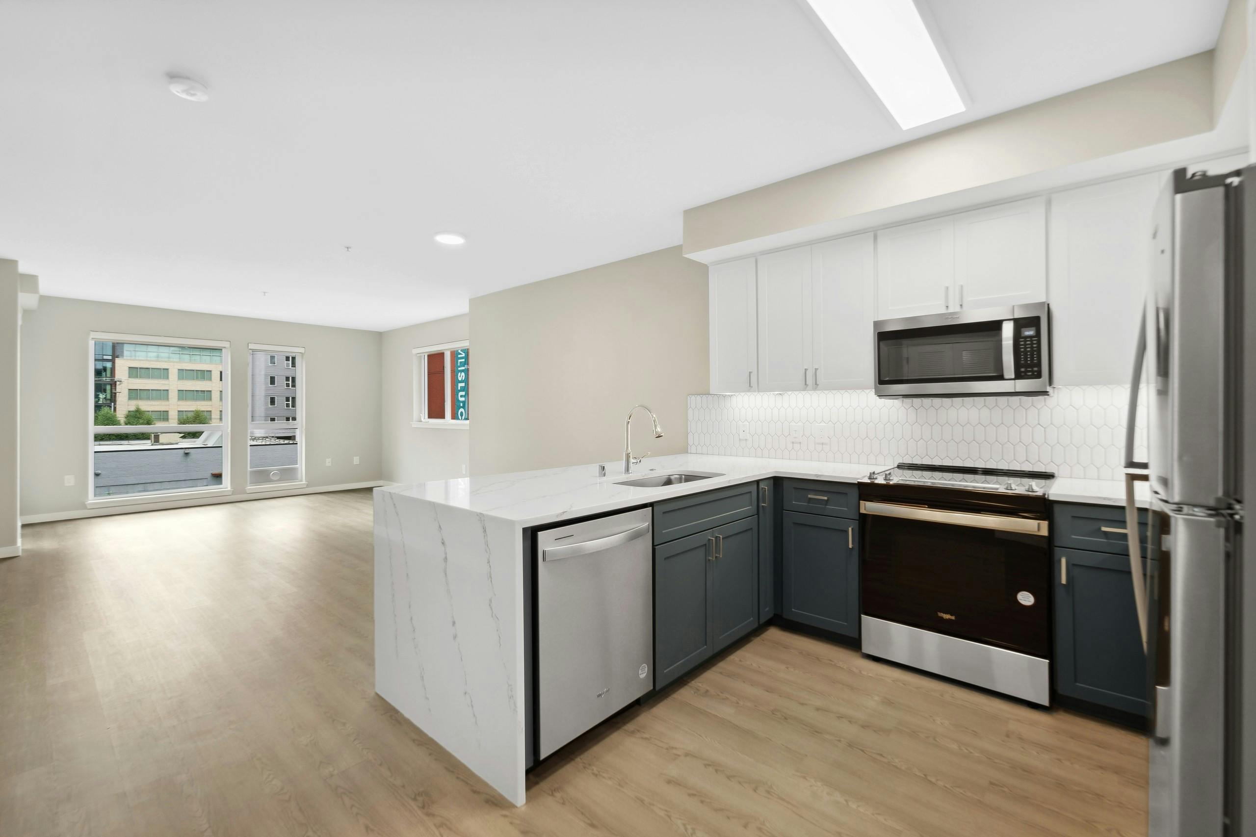 Kitchen at AMLI 535 with quartz countertop and stainless steel refrigerator and a view into living room with plank flooring