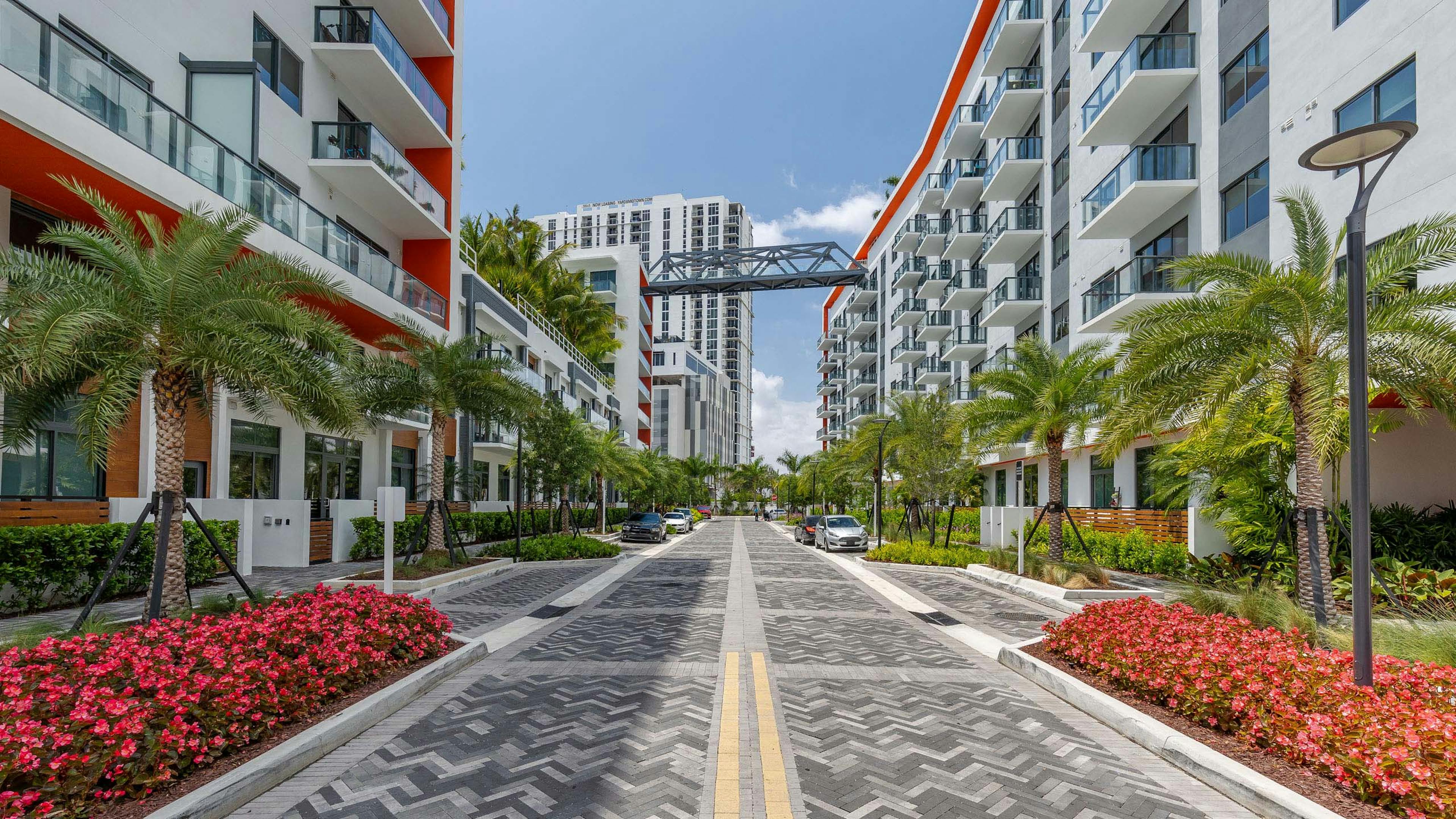 AMLI Midtown Miami apartments with gray herringbone pavers and white building facade and palm trees with bridge view