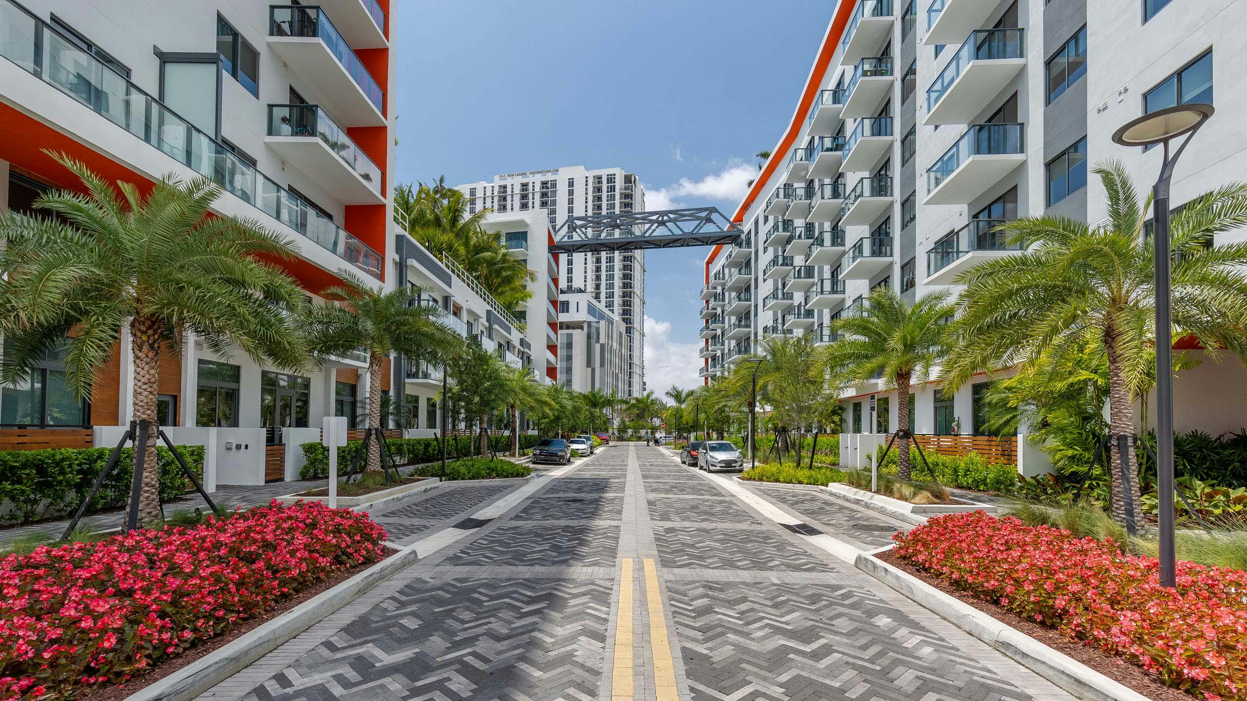 AMLI Midtown Miami apartments with gray herringbone pavers and white building facade and palm trees with bridge view