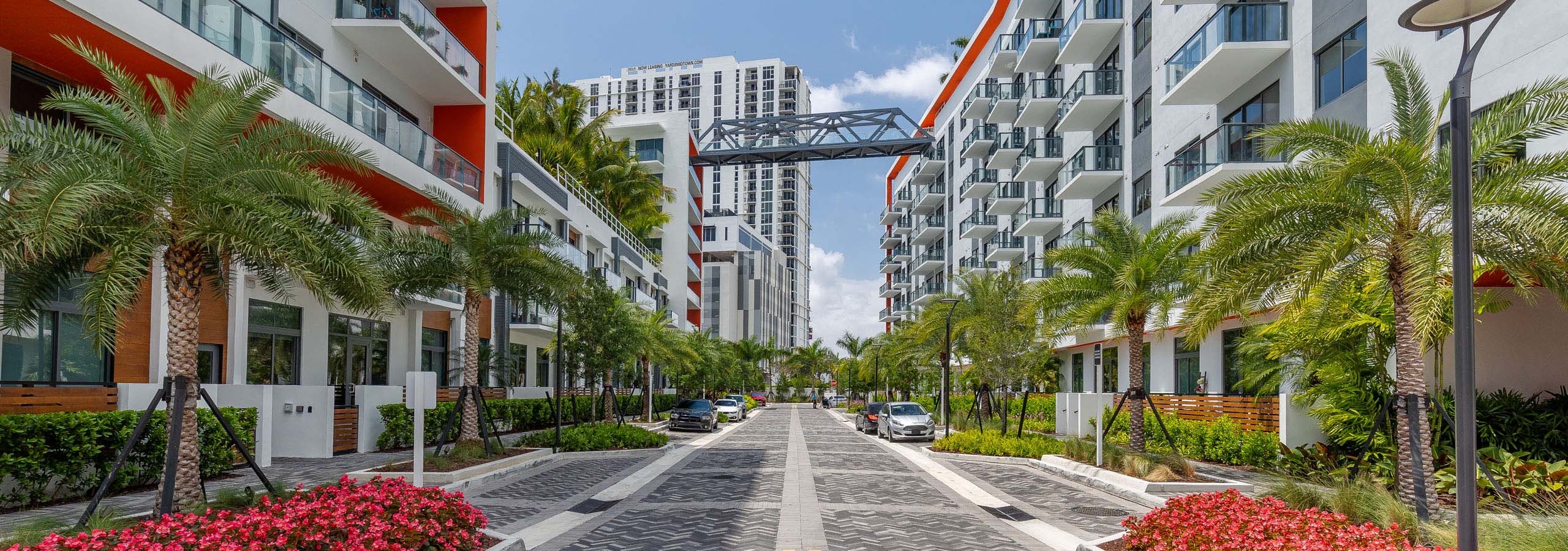 AMLI Midtown Miami apartments with gray herringbone pavers and white building facade and palm trees with bridge view