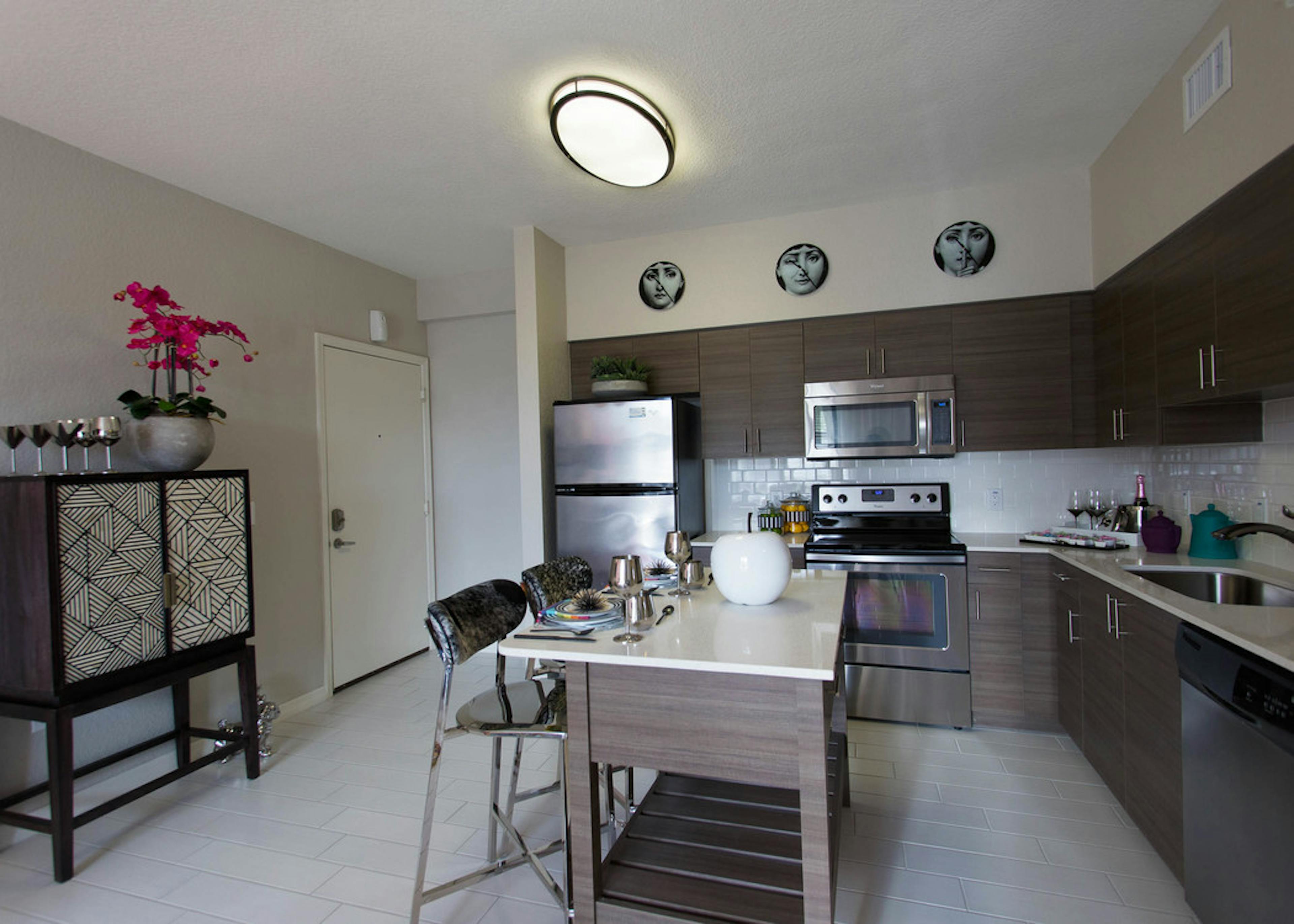  Interior view of AMLI Dadeland apartment island kitchen with stainless steel appliances and dark wood cabinetry