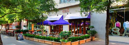 AMLI Downtown exterior showing mannequins in a retail shop window and an outdoor dining area with blue umbrellas and shrubs