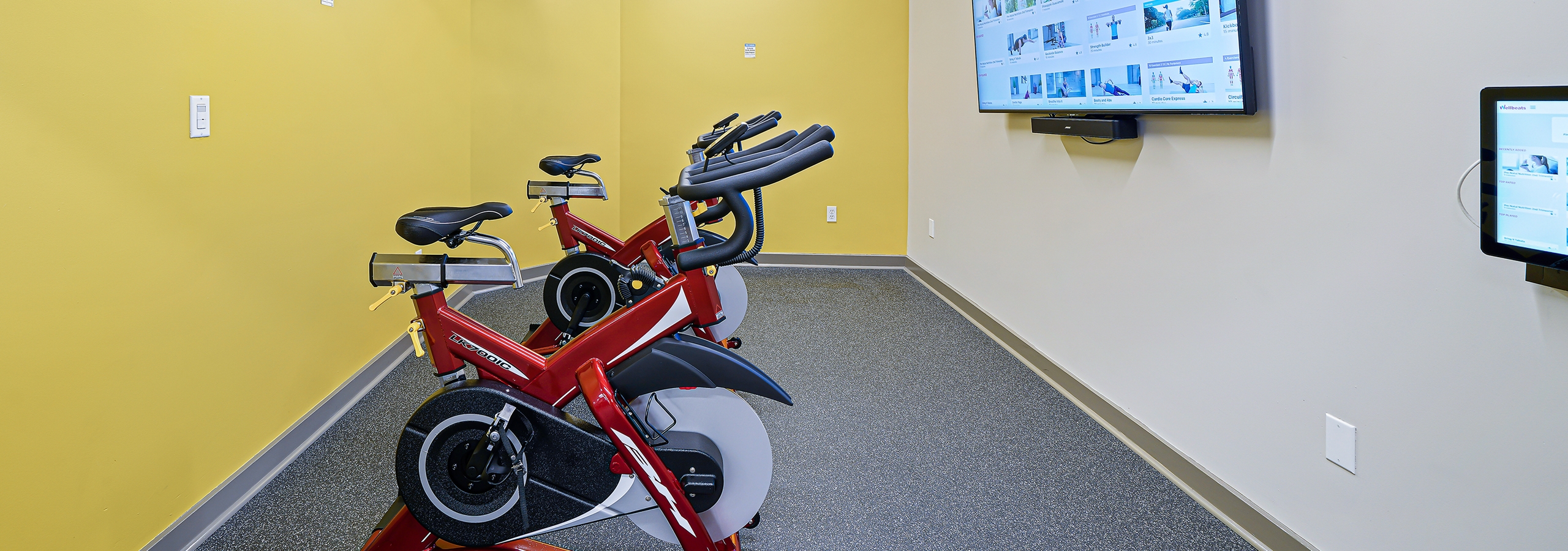 Bright yellow walls behind two spin bikes facing fitness on demand TV at fitness center at AMLI Bellevue Park apartments