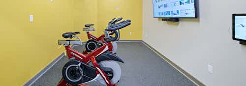 Bright yellow walls behind two spin bikes facing fitness on demand TV at fitness center at AMLI Bellevue Park apartments