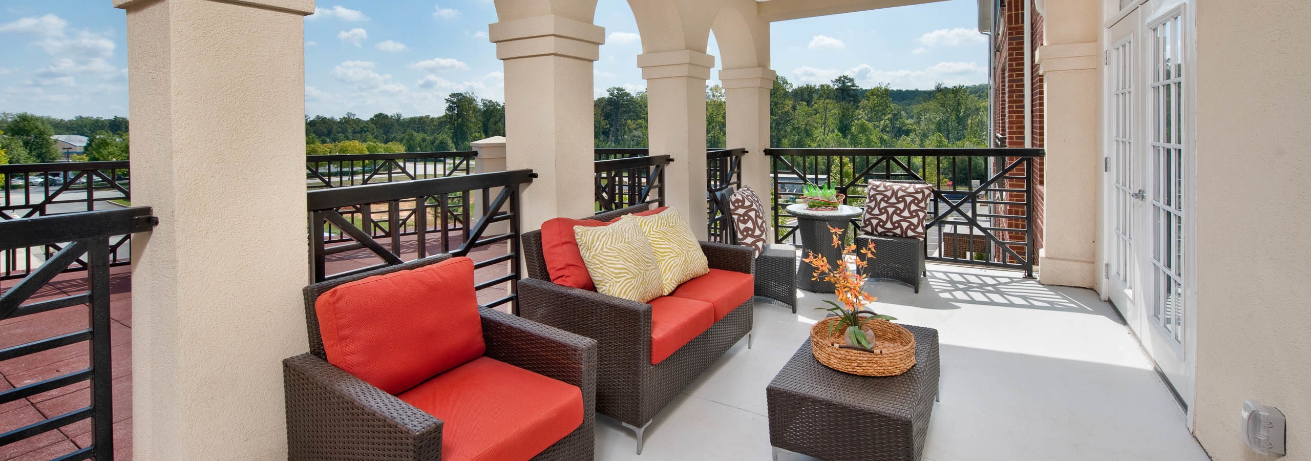 Spacious patio area at AMLI North Point with red wicker lounge chairs fenced in with scenic views in the background