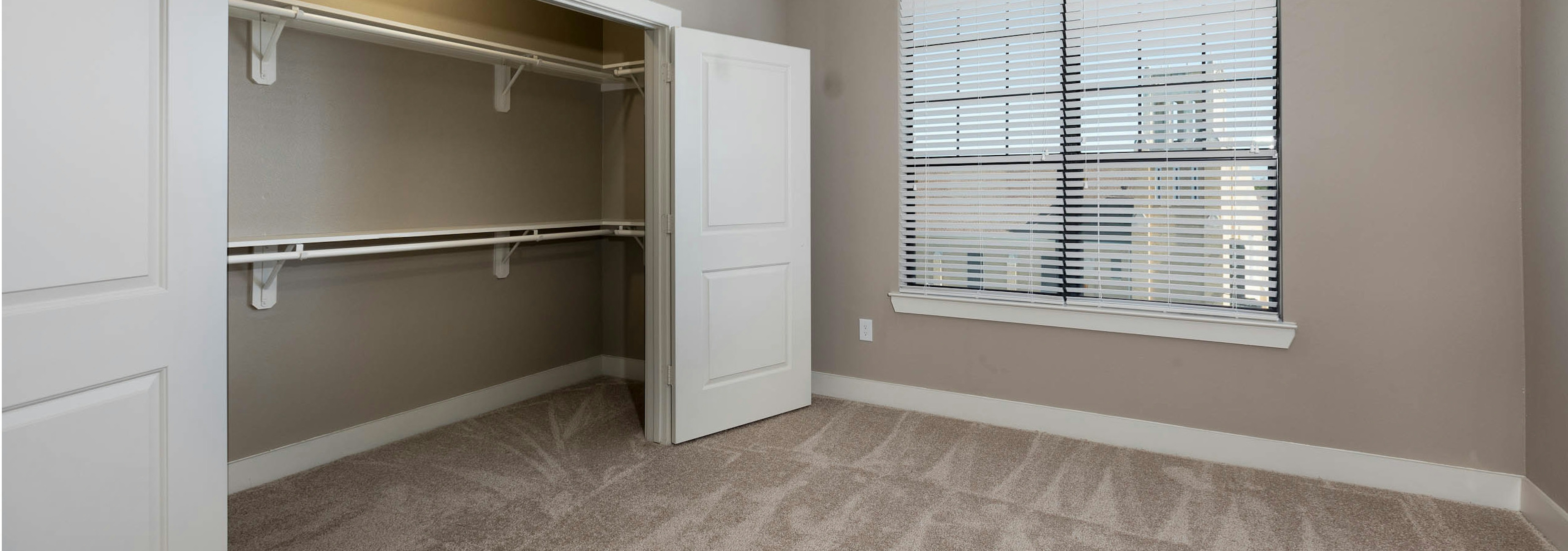 Interior of AMLI Eastside bedroom with open doors revealing spacious closet with grey walls and a window with daytime view