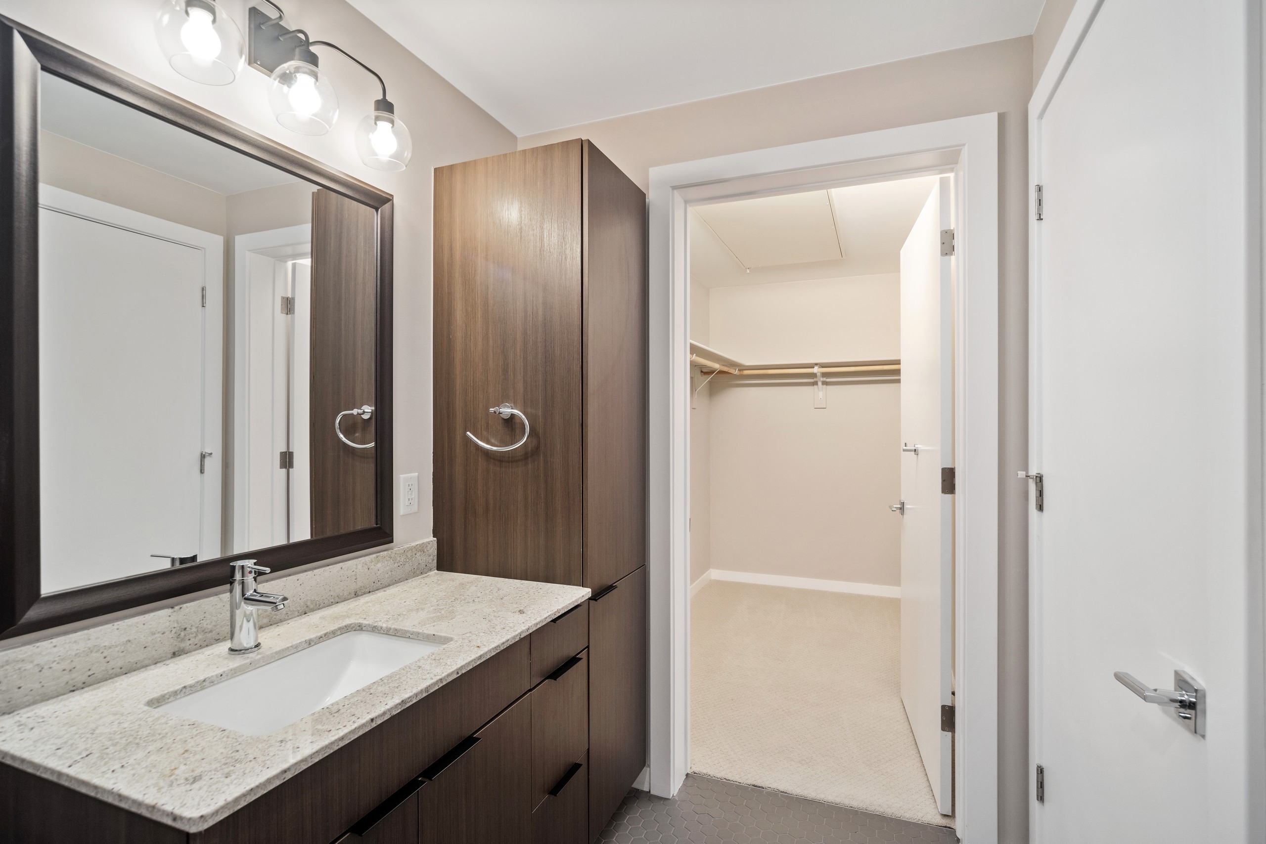 AMLI at Uptown apartment bathroom with dark cabinetry and a light countertop vanity connecting to spacious walk in closet