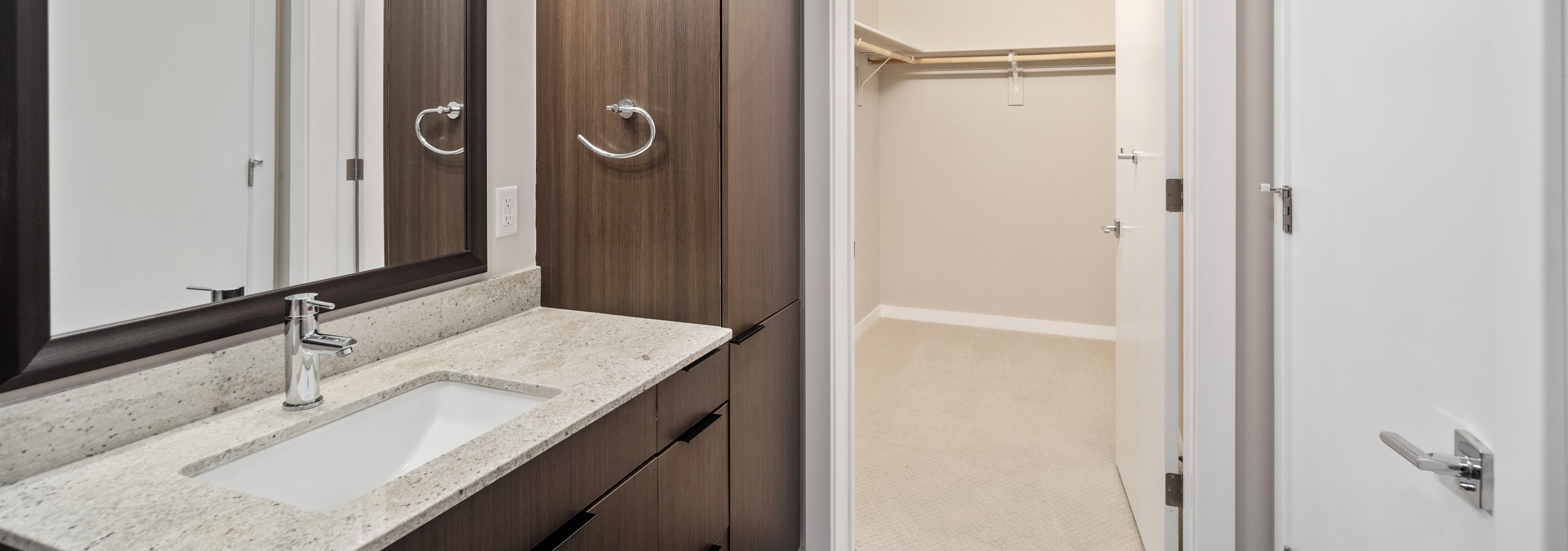 AMLI at Uptown apartment bathroom with dark cabinetry and a light countertop vanity connecting to spacious walk in closet