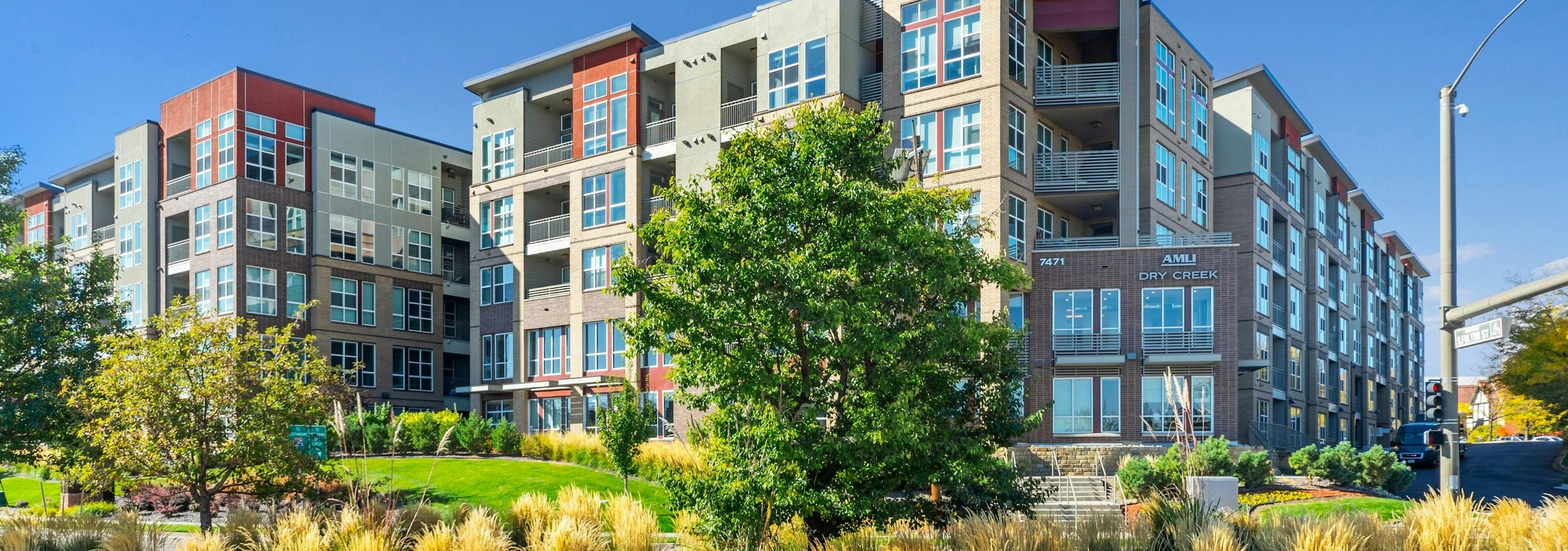 Exterior view of AMLI Dry Creek apartments showcasing several balconies and windows and green grass and trees and blue sky