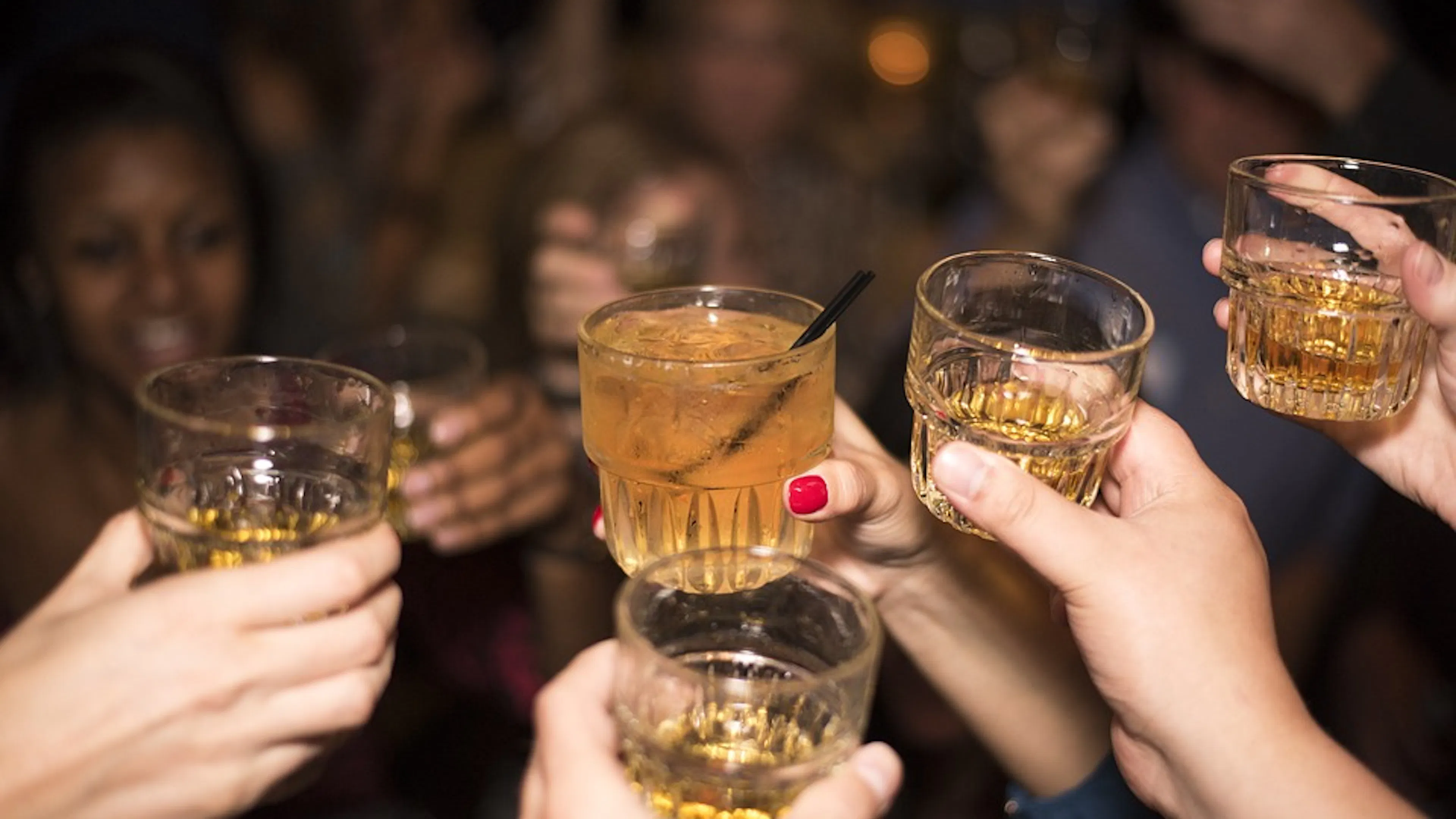 A group of people toasting each other with whiskey glasses in their hands filled with whiskey
