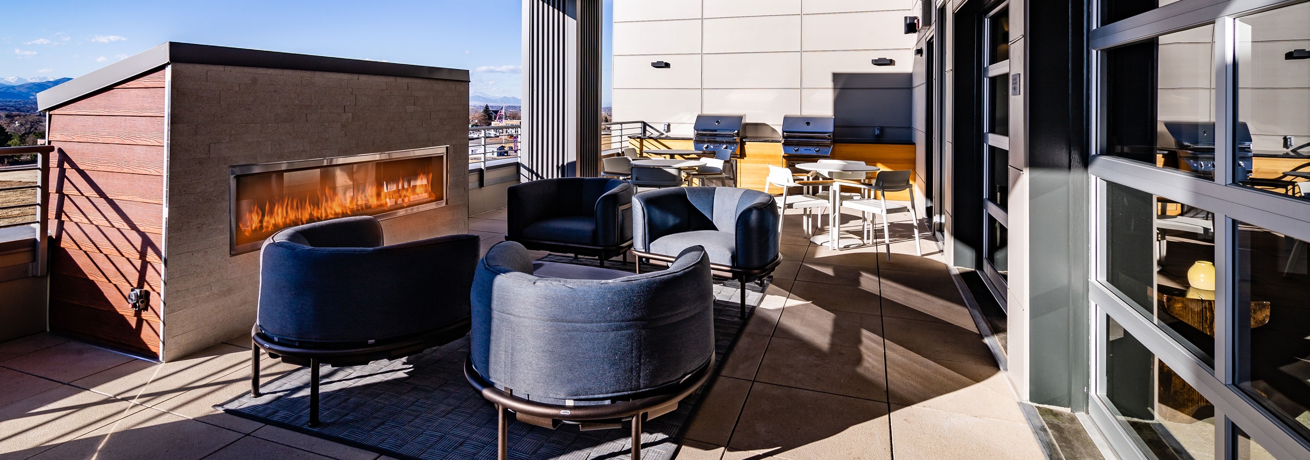 Daytime view of outdoor rooftop lounge with grilling station and blue designer chairs at AMLI Littleton Village apartments