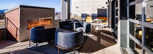 Daytime view of outdoor rooftop lounge with grilling station and blue designer chairs at AMLI Littleton Village apartments
