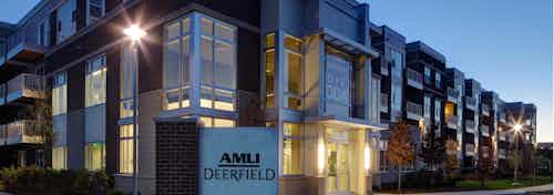 Dusk exterior view of the corner of the AMLI Deerfield main building with landscaping and interior lights beaming