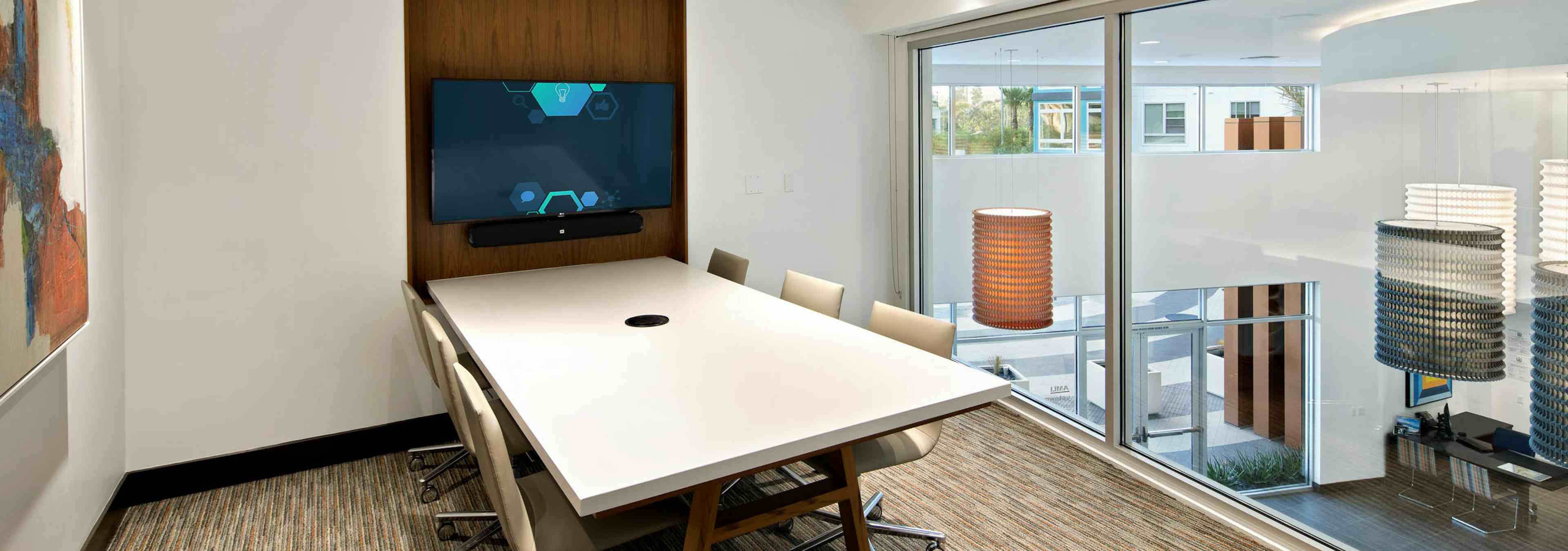 Interior of conference room at AMLI Uptown Orange apartments with white long table and six beige chairs and big screen TV