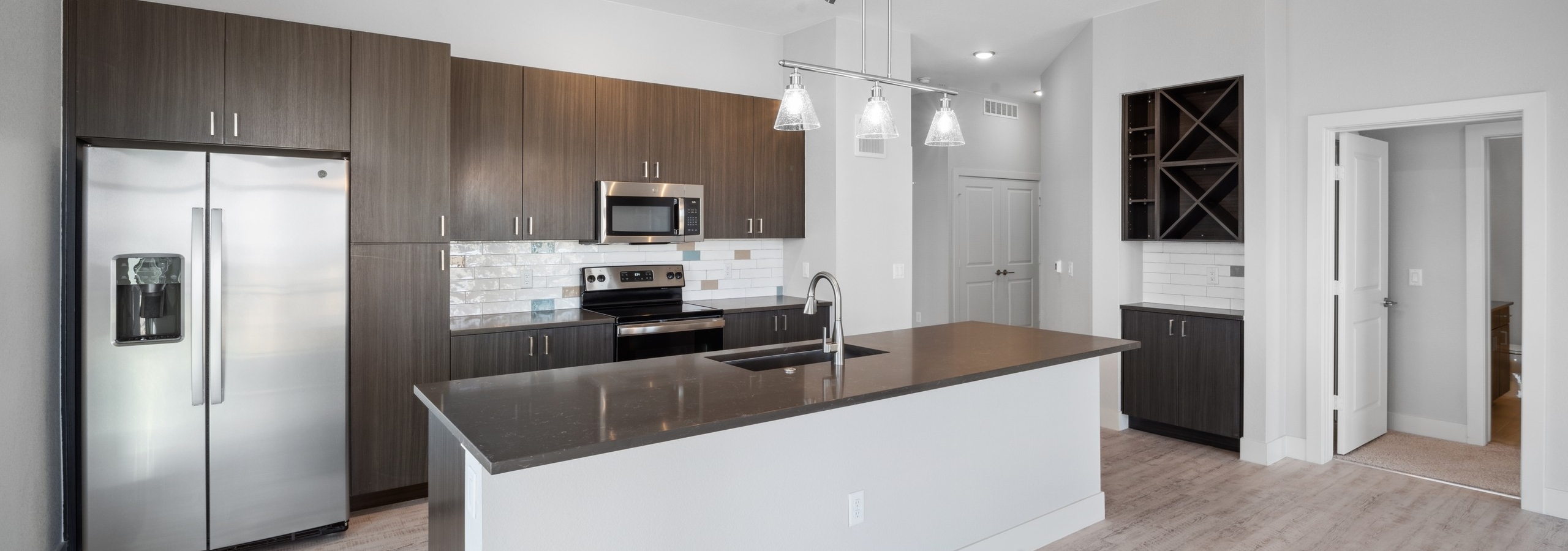 Kitchen at AMLI RiNo with large island and dark quartz countertops with brown woodgrain cabinets and built-in shelves