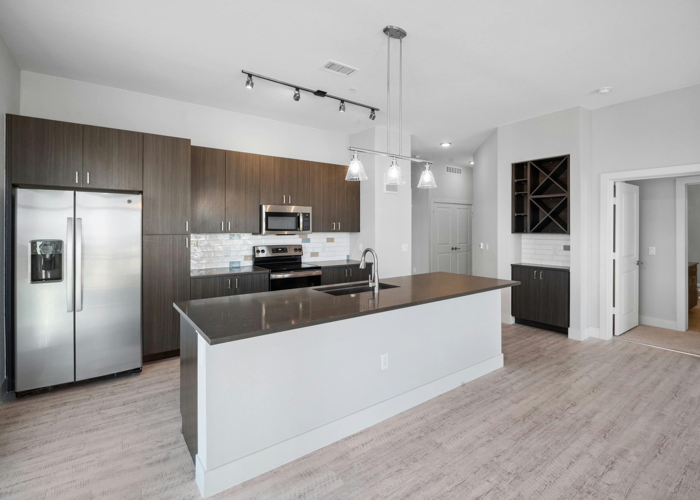 Kitchen at AMLI RiNo with large island and dark quartz countertops with brown woodgrain cabinets and built-in shelves