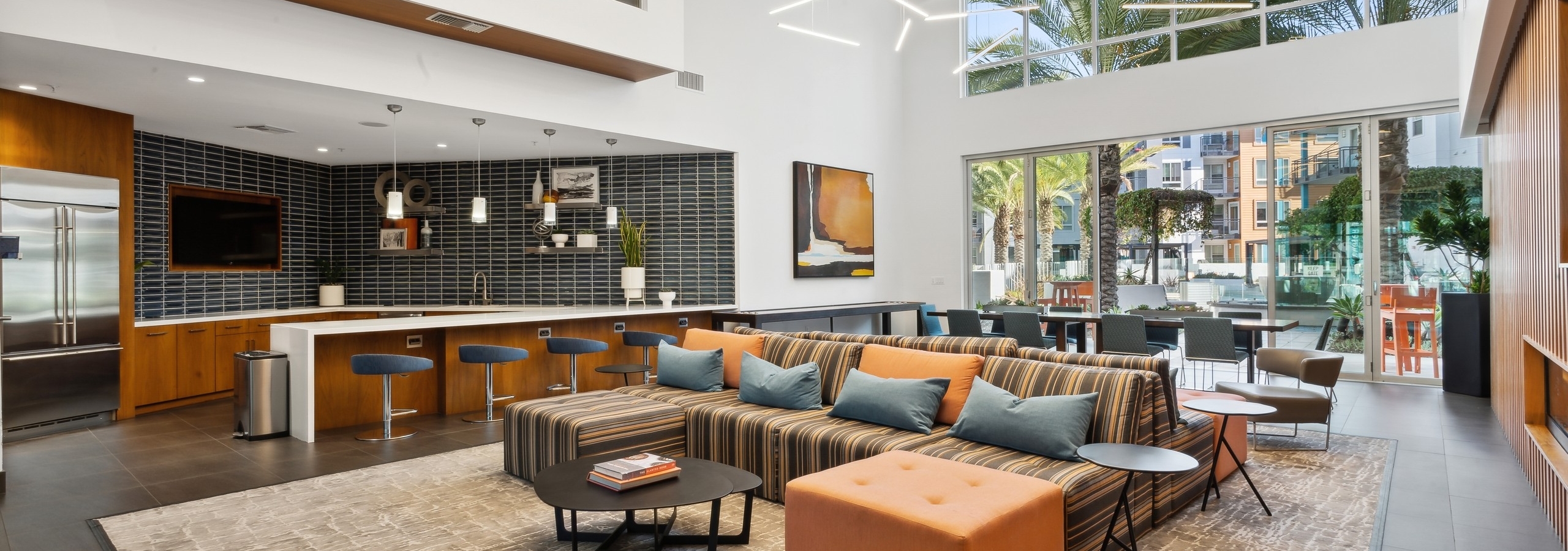 Furnished resident clubroom with serving kitchen and glass doors facing the pool area at AMLI Uptown Orange apartments