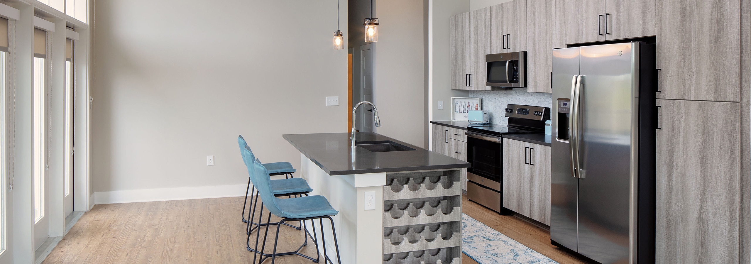 AMLI Decatur kitchen with light wood cabinetry and large windows with an island with blue barstools and a built in wine rack