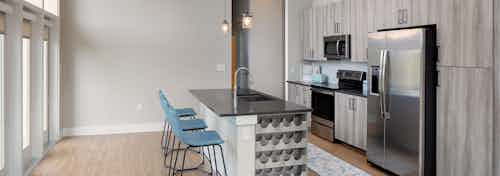 AMLI Decatur kitchen with light wood cabinetry and large windows with an island with blue barstools and a built in wine rack